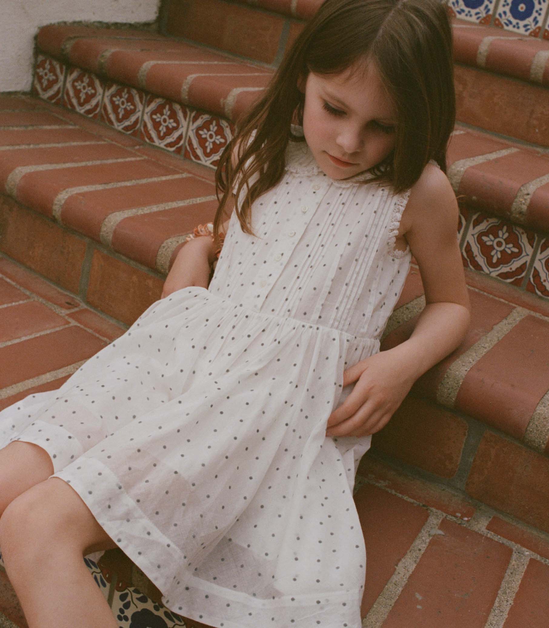 Young girl in a white dress sitting on a patterned bench.