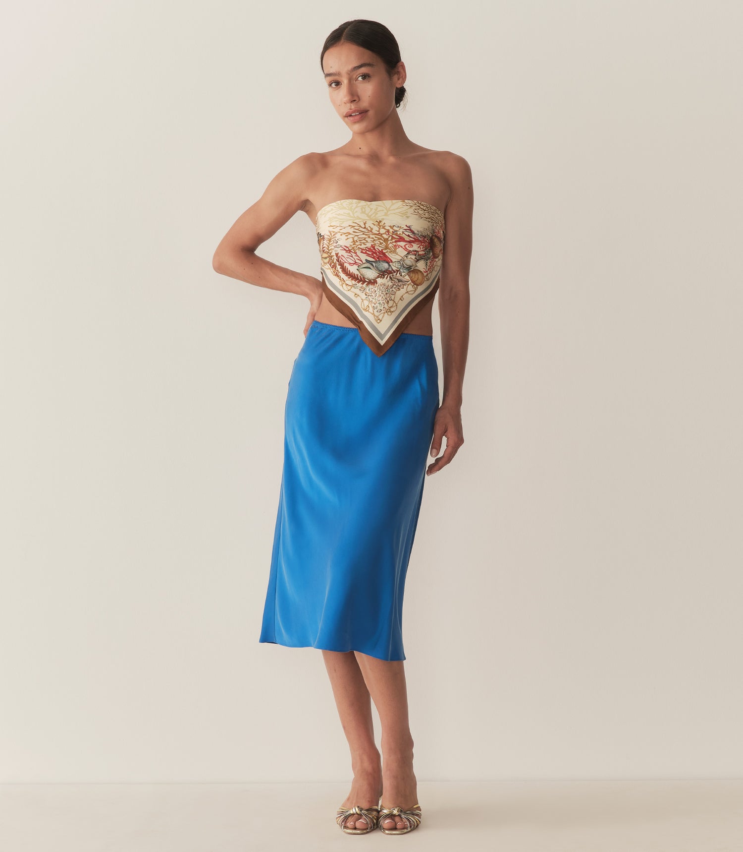 Zahara is wearing a blue midi skirt paired with a bandana top and metallic kitten heels.