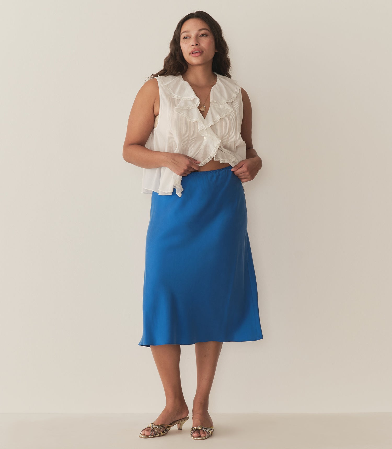 Alana is wearing a blue midi skirt paired with a white sleeveless top and metallic kitten heels.