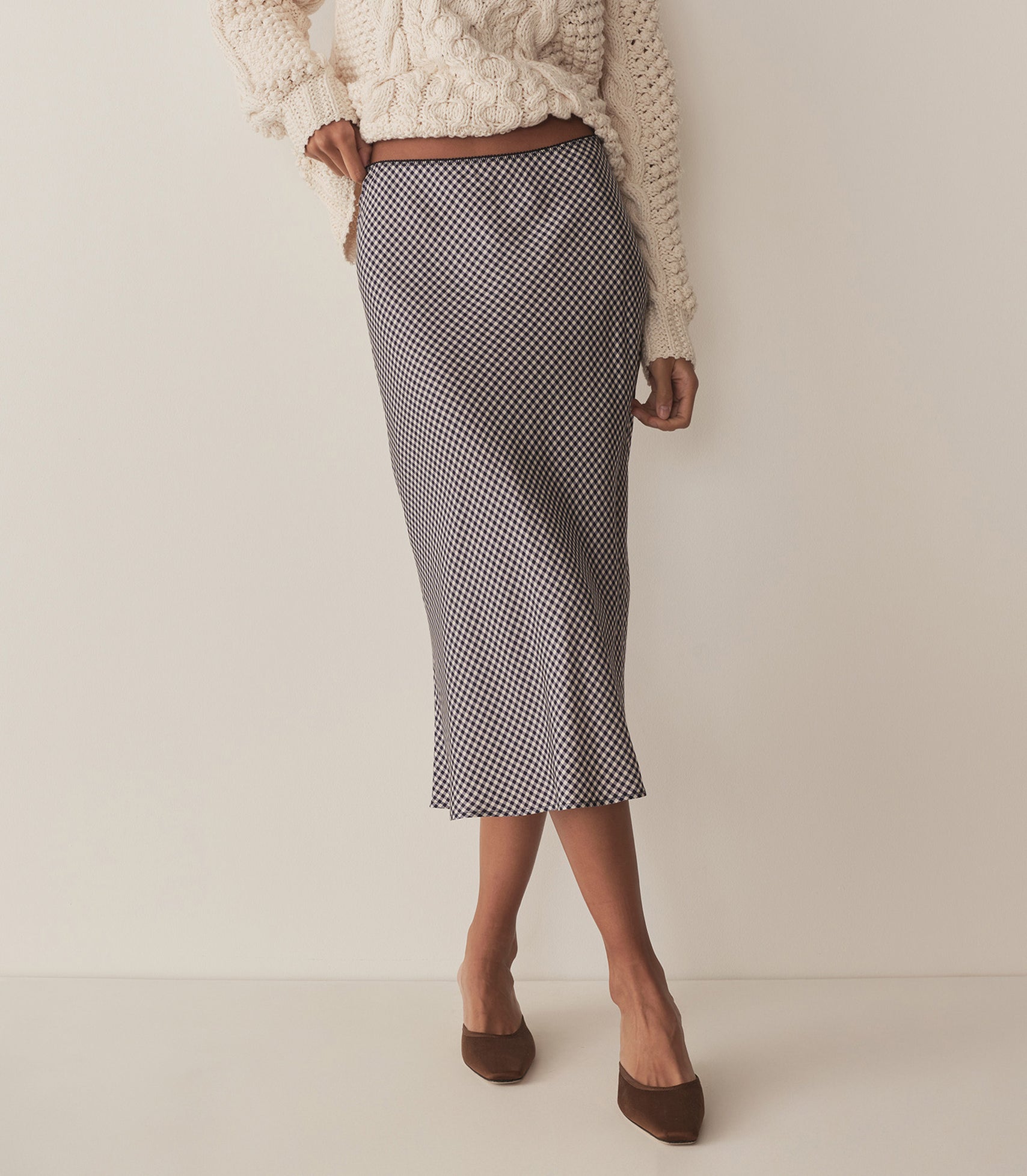 Rocio wears a navy and white gingham skirt with a chunky white sweater and chocolate brown heels.