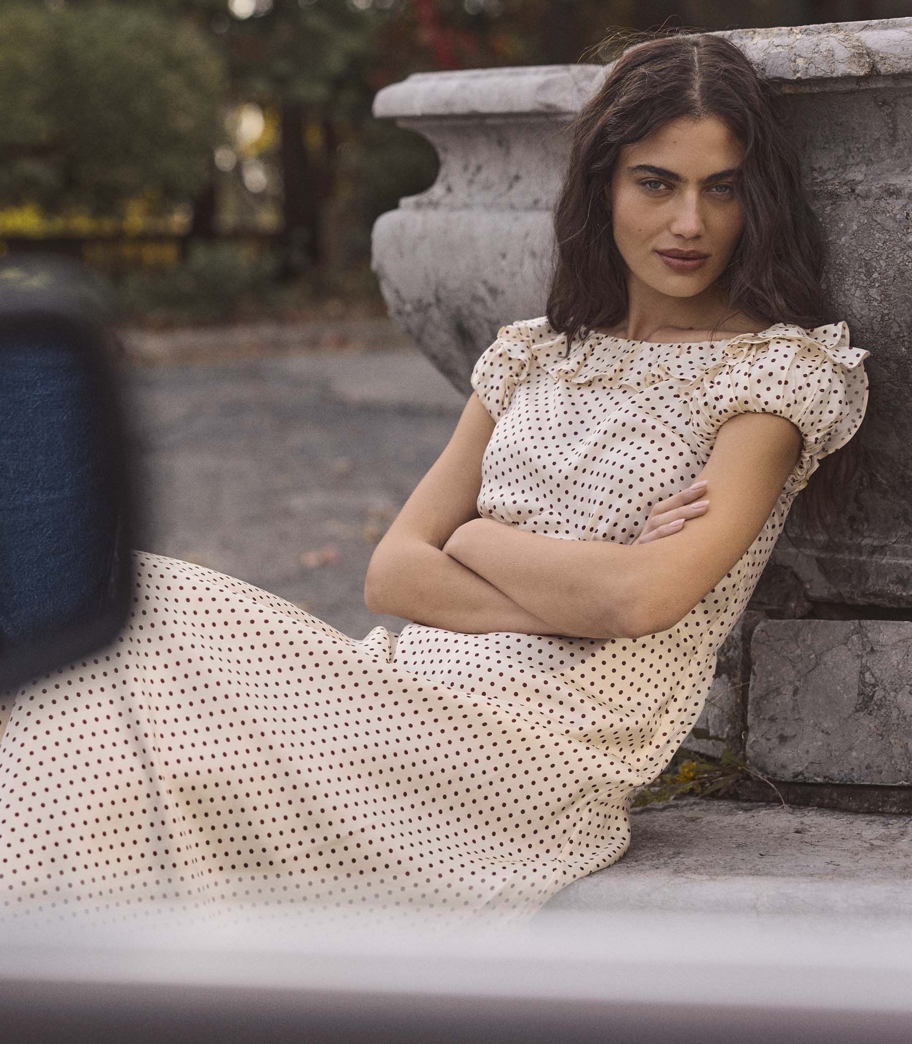 Woman in a polka dot dress sitting against a stone wall outdoors 1
