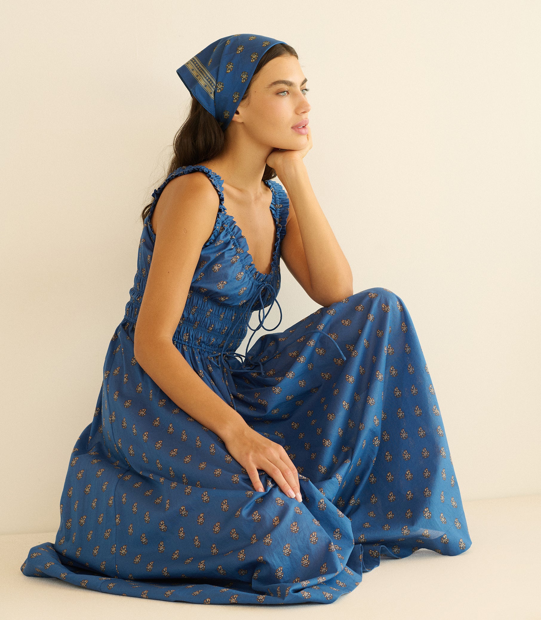 Woman wearing a blue paisley bandana with a matching dress on a beige background 1
