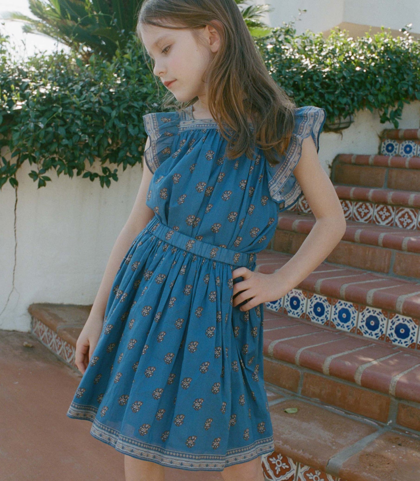 Young girl wearing a blue paisley skirt with a matching top outdoors.