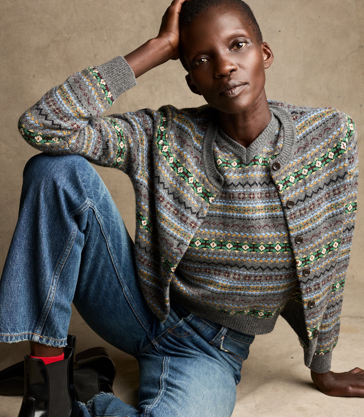 Person wearing a patterned sweater and jeans against a neutral background