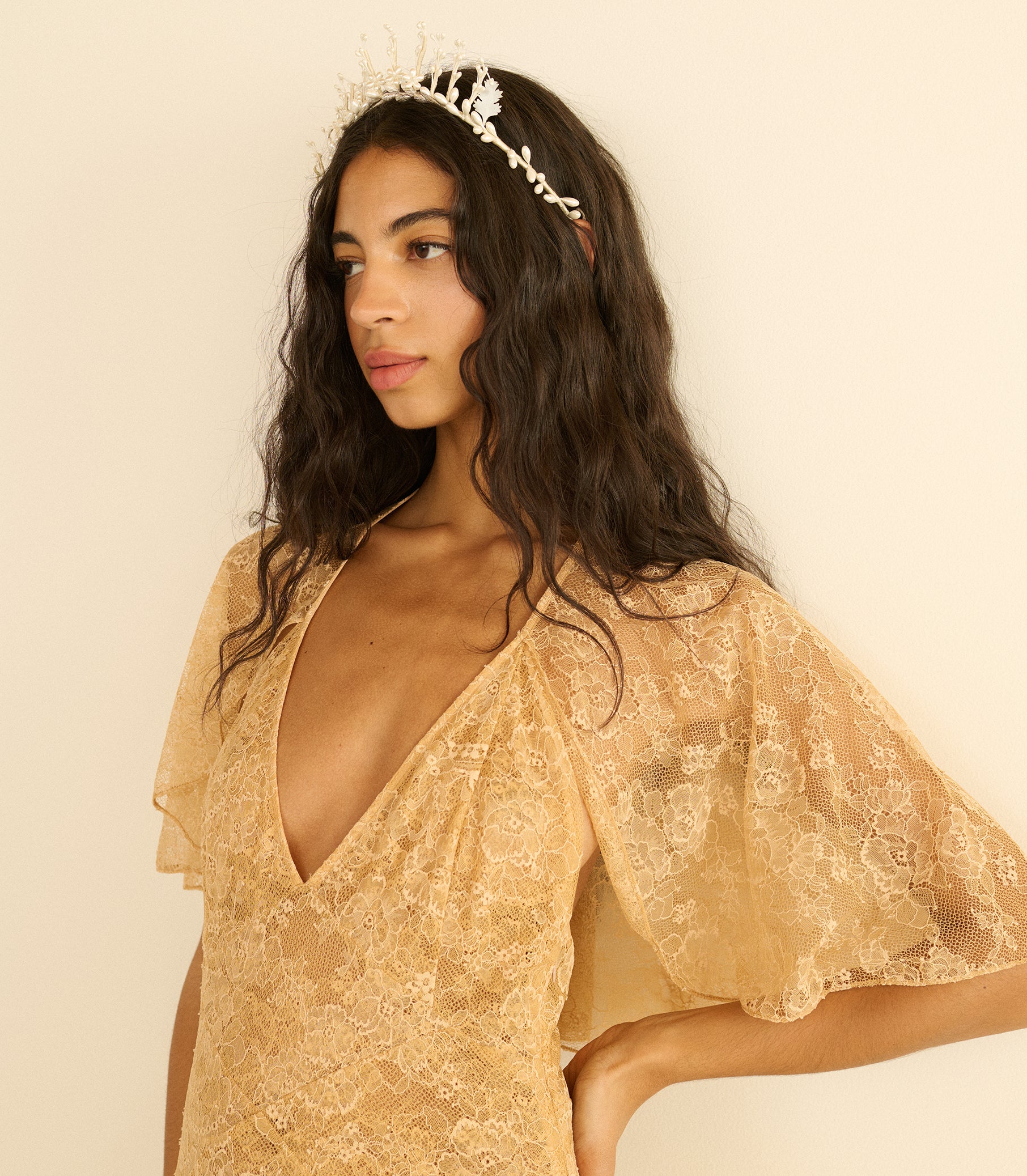 Woman wearing a gold lace dress with a plain background