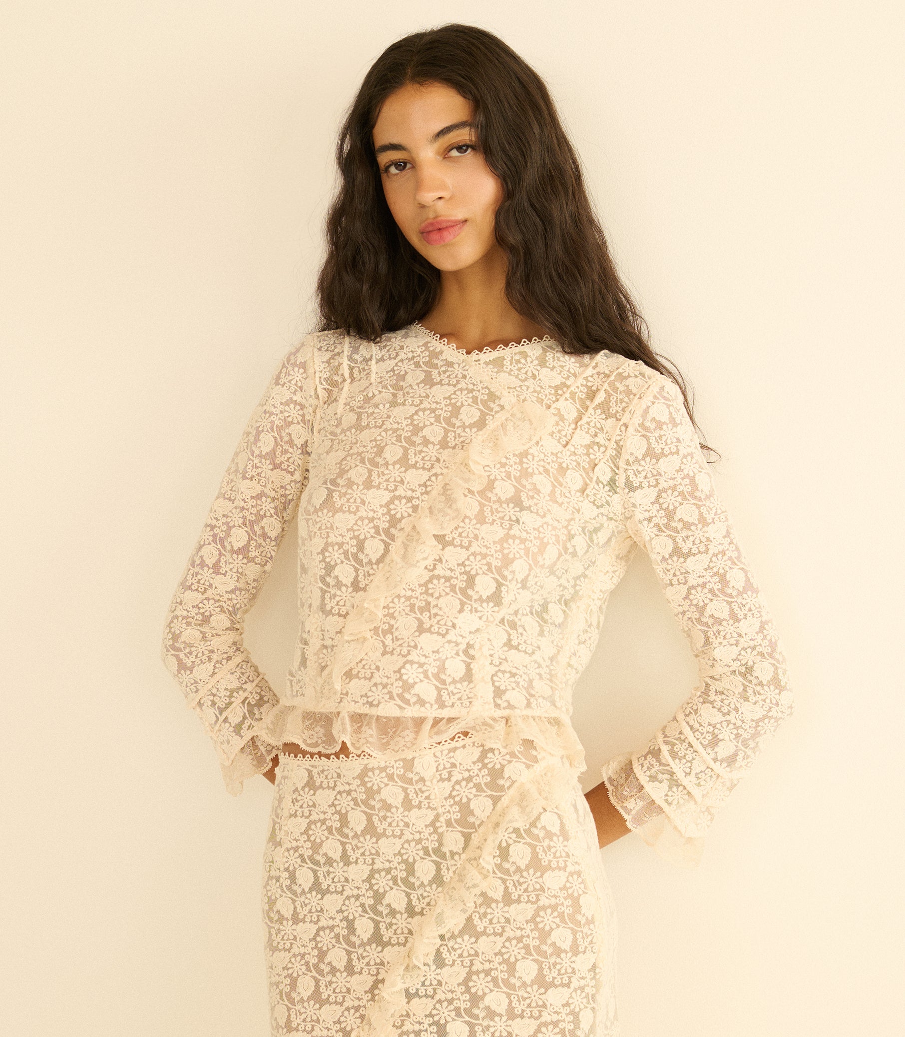 Woman wearing a cream lace outfit against a plain background