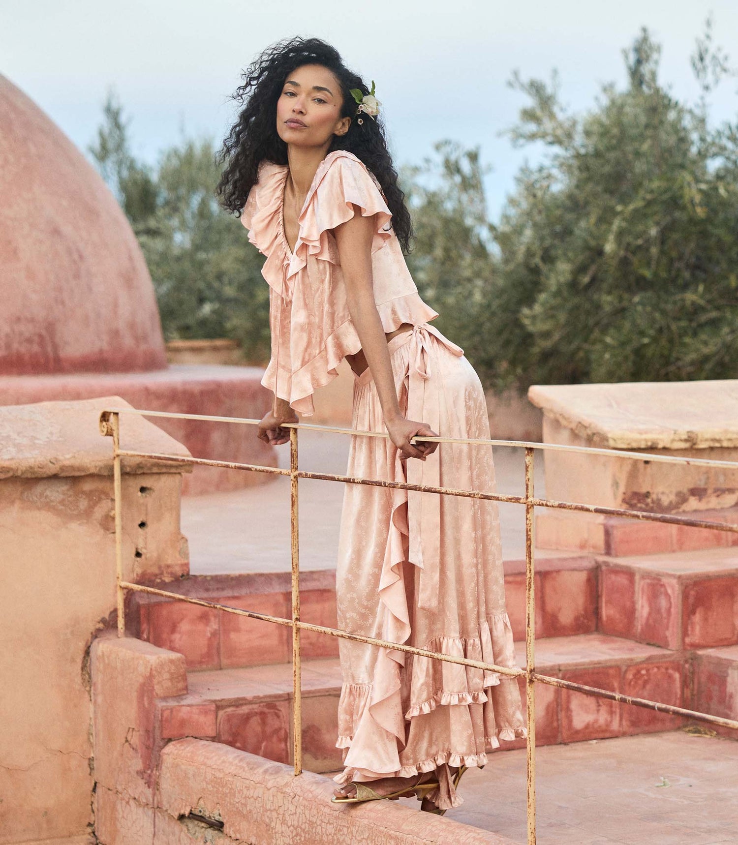 Woman in a flowing peach matching set standing on stone steps with greenery in the background