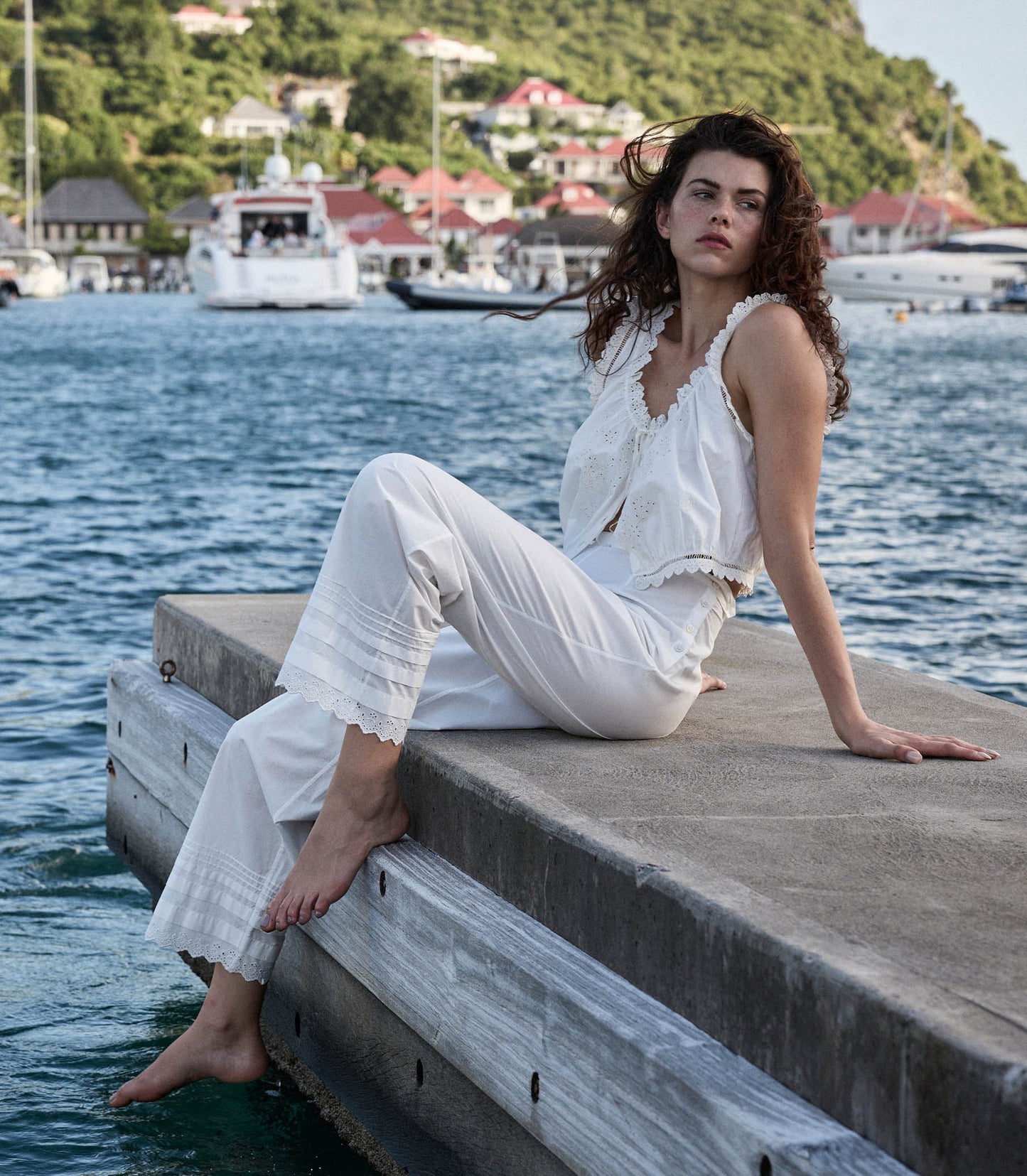 Georgia is wearing white pants and a white blouse in front of a lake.