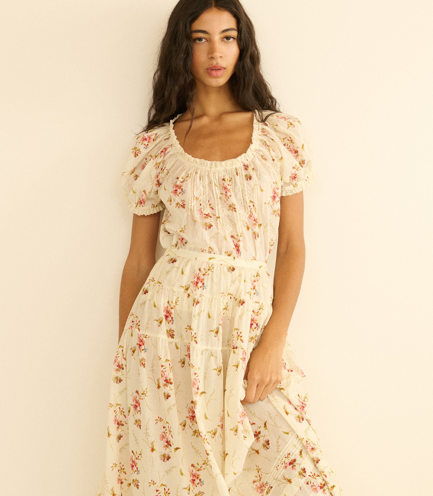Woman wearing a floral blouse and matching skirt against a plain background