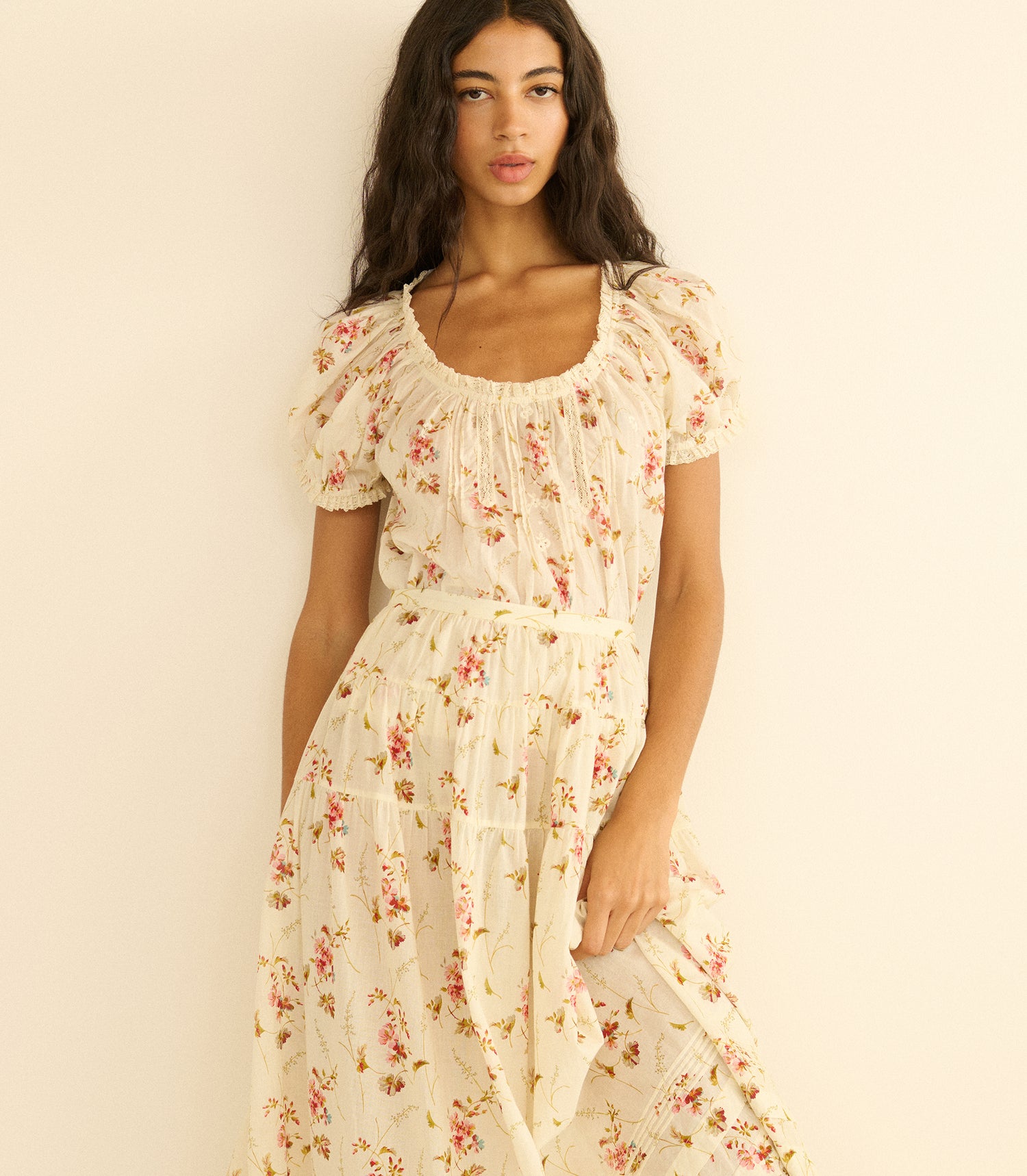 Woman wearing a floral blouse and matching skirt against a plain background