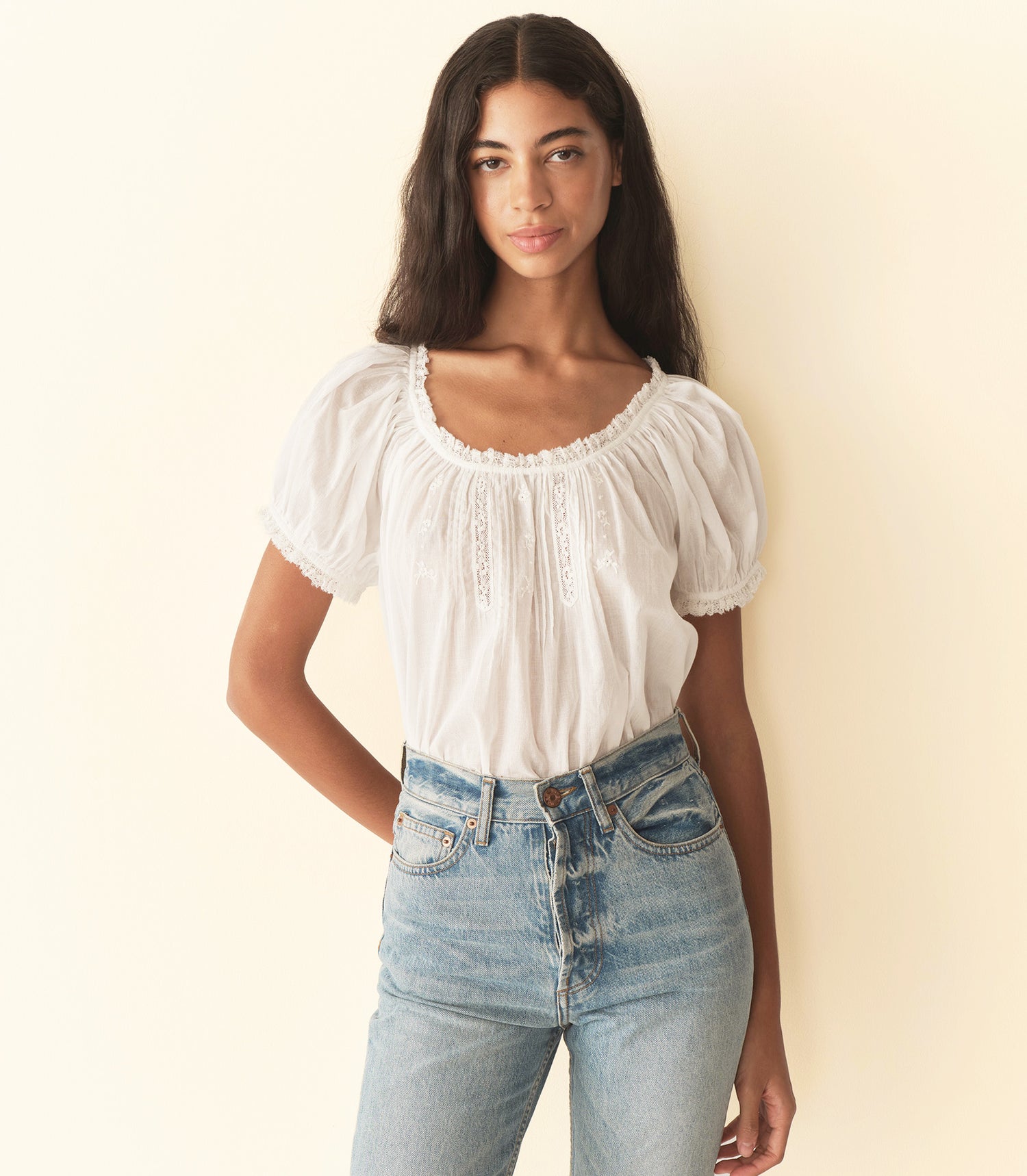 Woman wearing a white blouse and blue jeans against a plain background