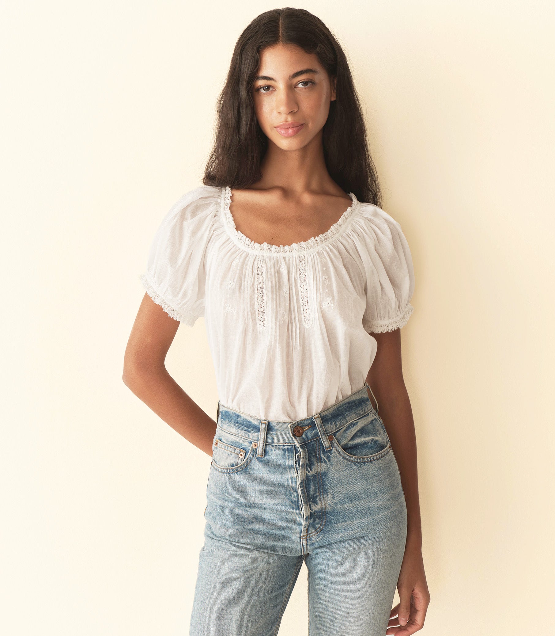 Woman wearing a white blouse and blue jeans against a plain background 1
