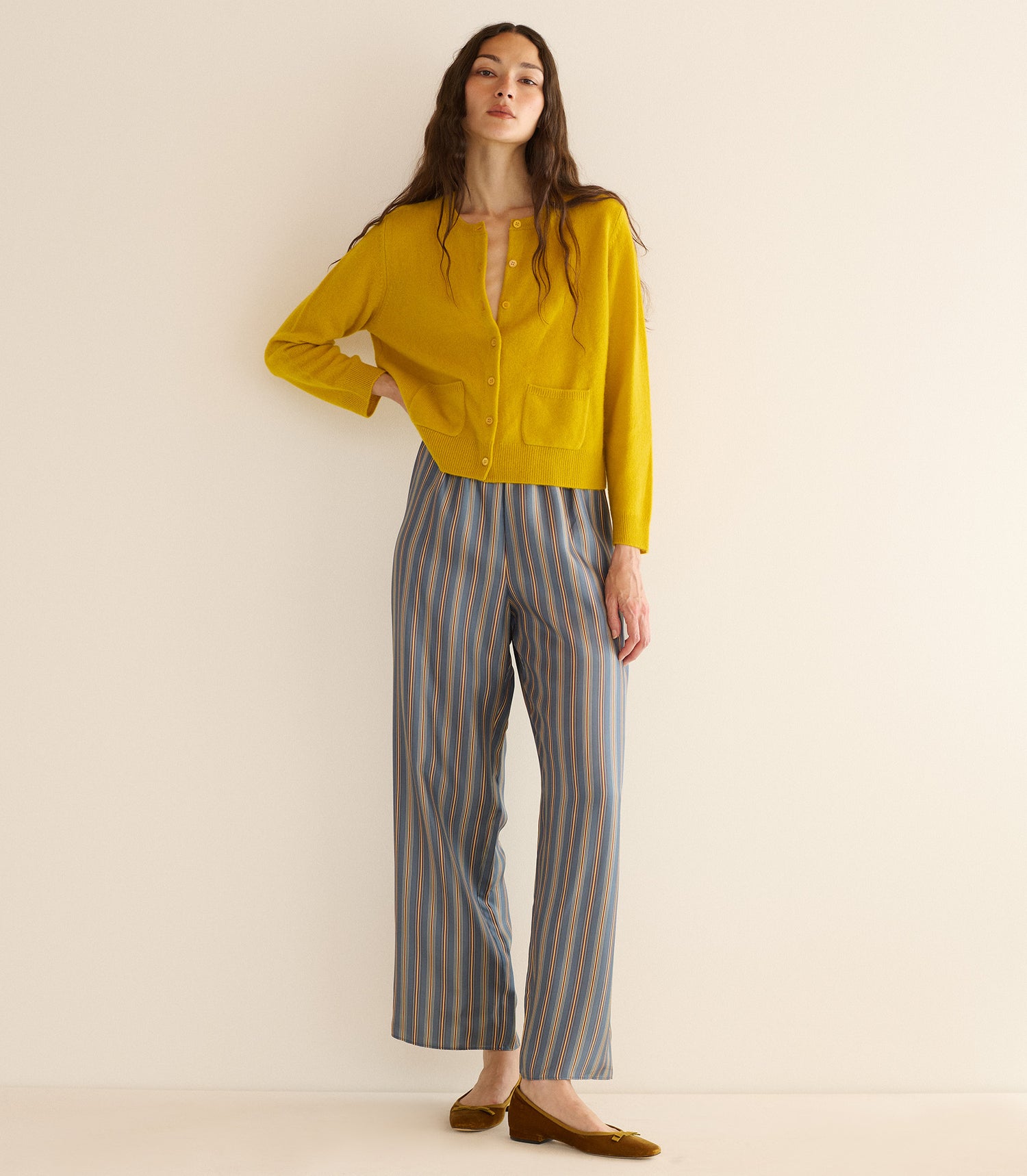 Woman wearing a yellow top and striped pants on a beige background