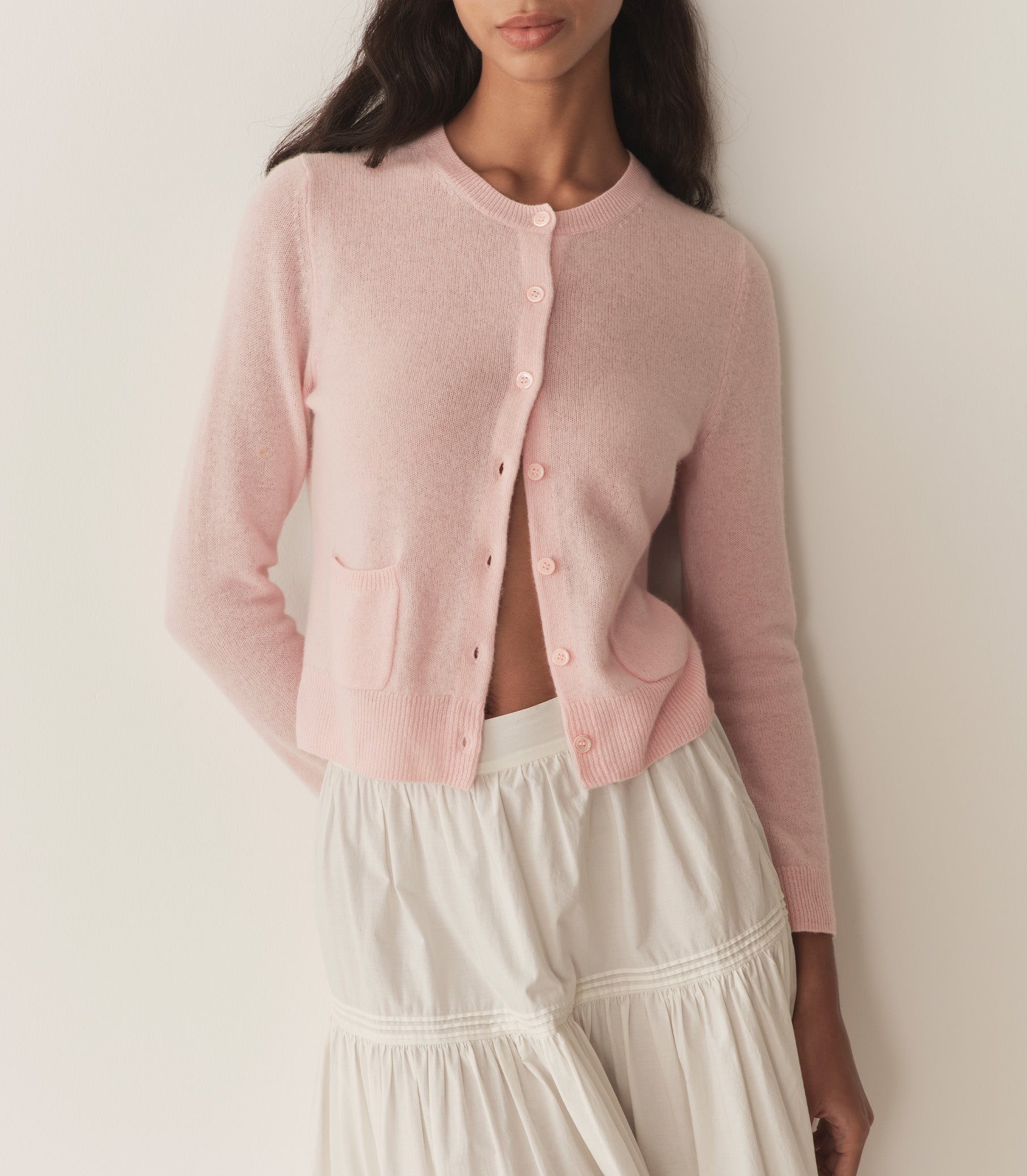 Zahara wears a light pink long sleeve cardigan with a long white skirt.