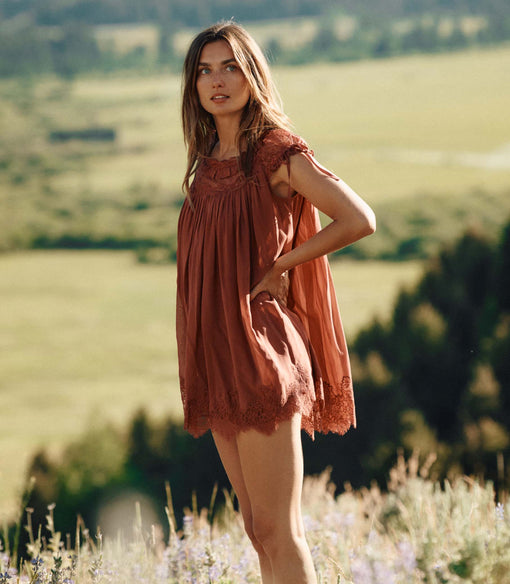 Woman in a rust-colored lace dress standing in a field with a scenic background