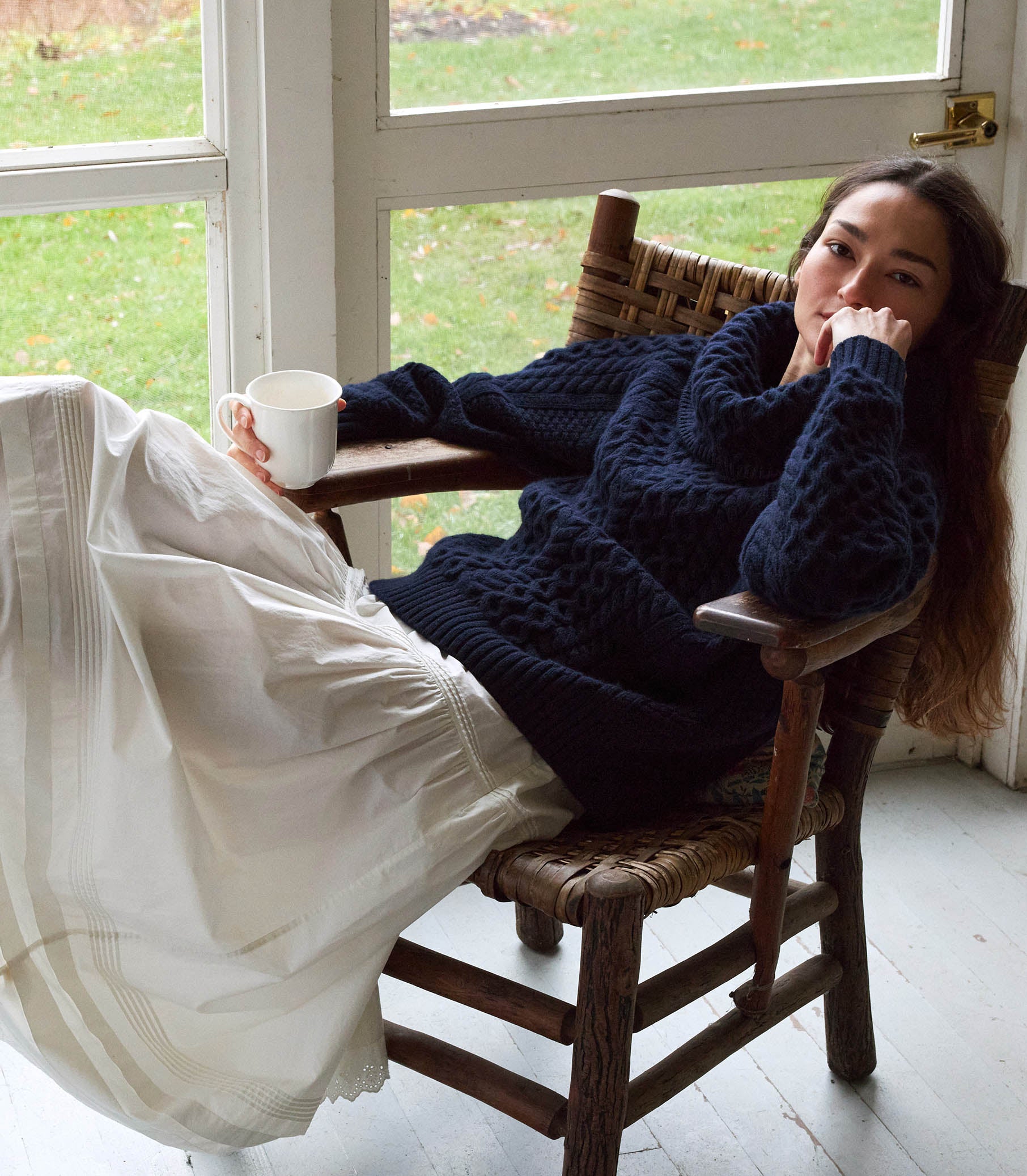 A person sitting in a chair, wearing a navy blue knitted sweater and white skirt. 