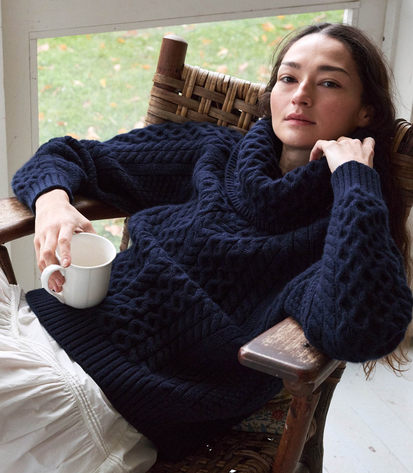 A person sitting in a chair, wearing a navy blue knitted sweater and white skirt. 