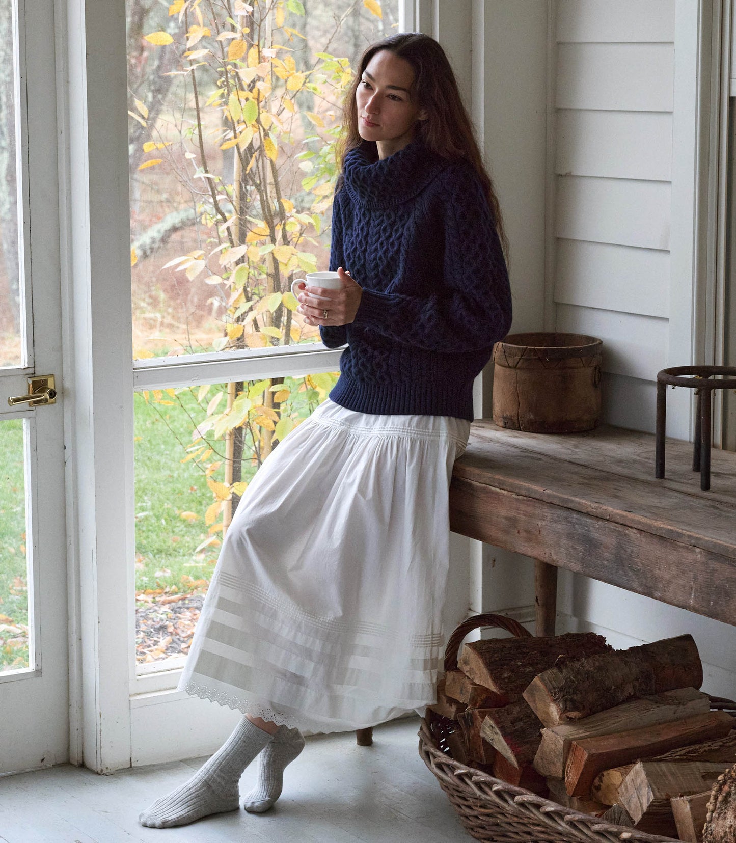 A person sitting in a chair, wearing a navy blue knitted sweater and white skirt. 