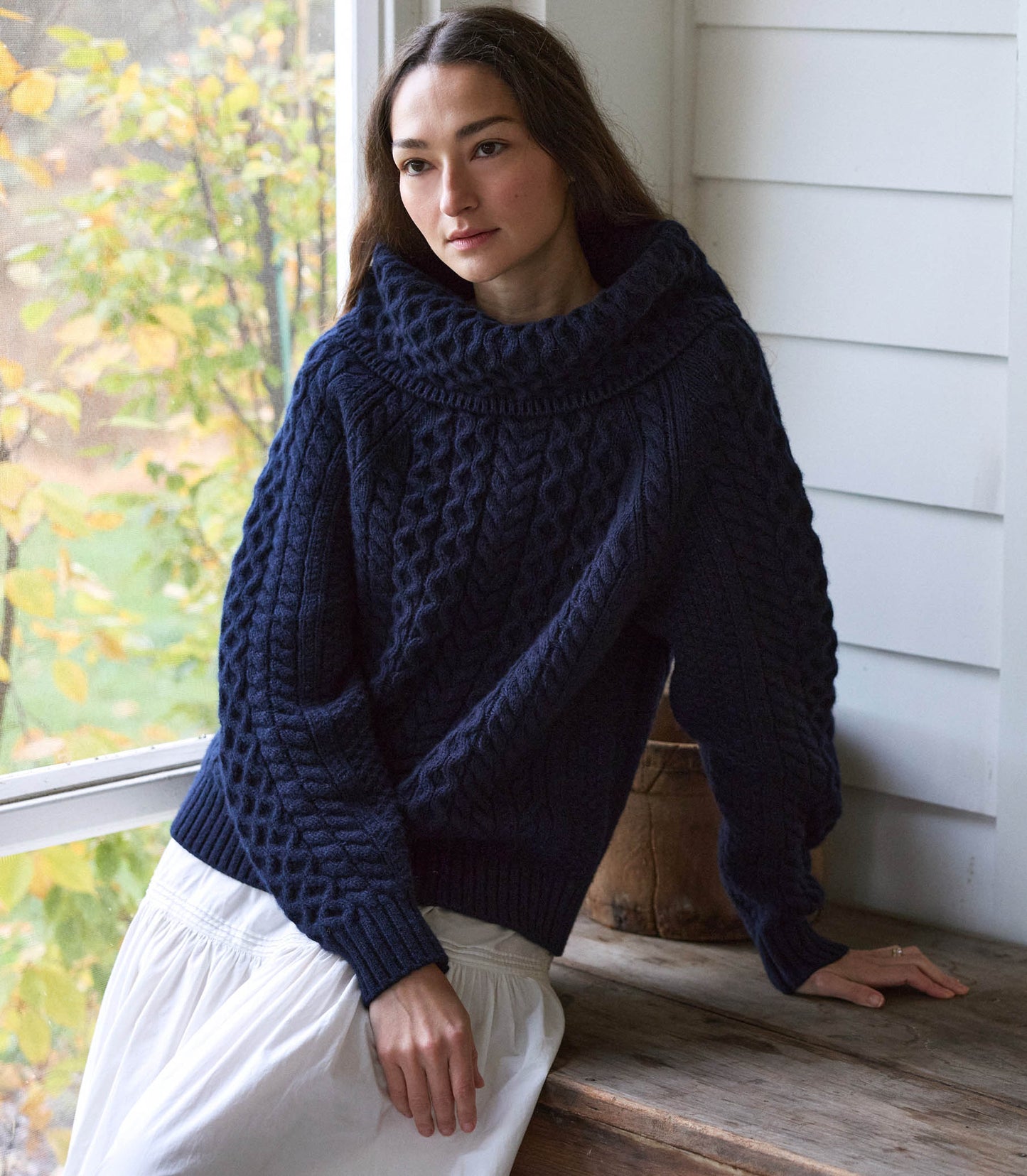 A person sitting in a chair, wearing a navy blue knitted sweater and white skirt. 