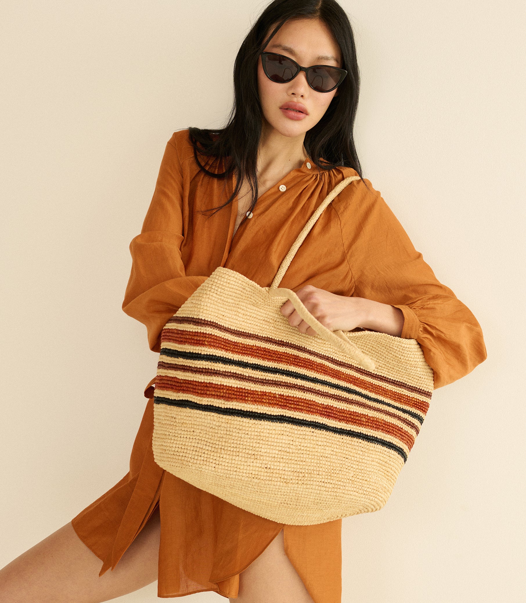 Woman holding a striped raffia bag against a beige background