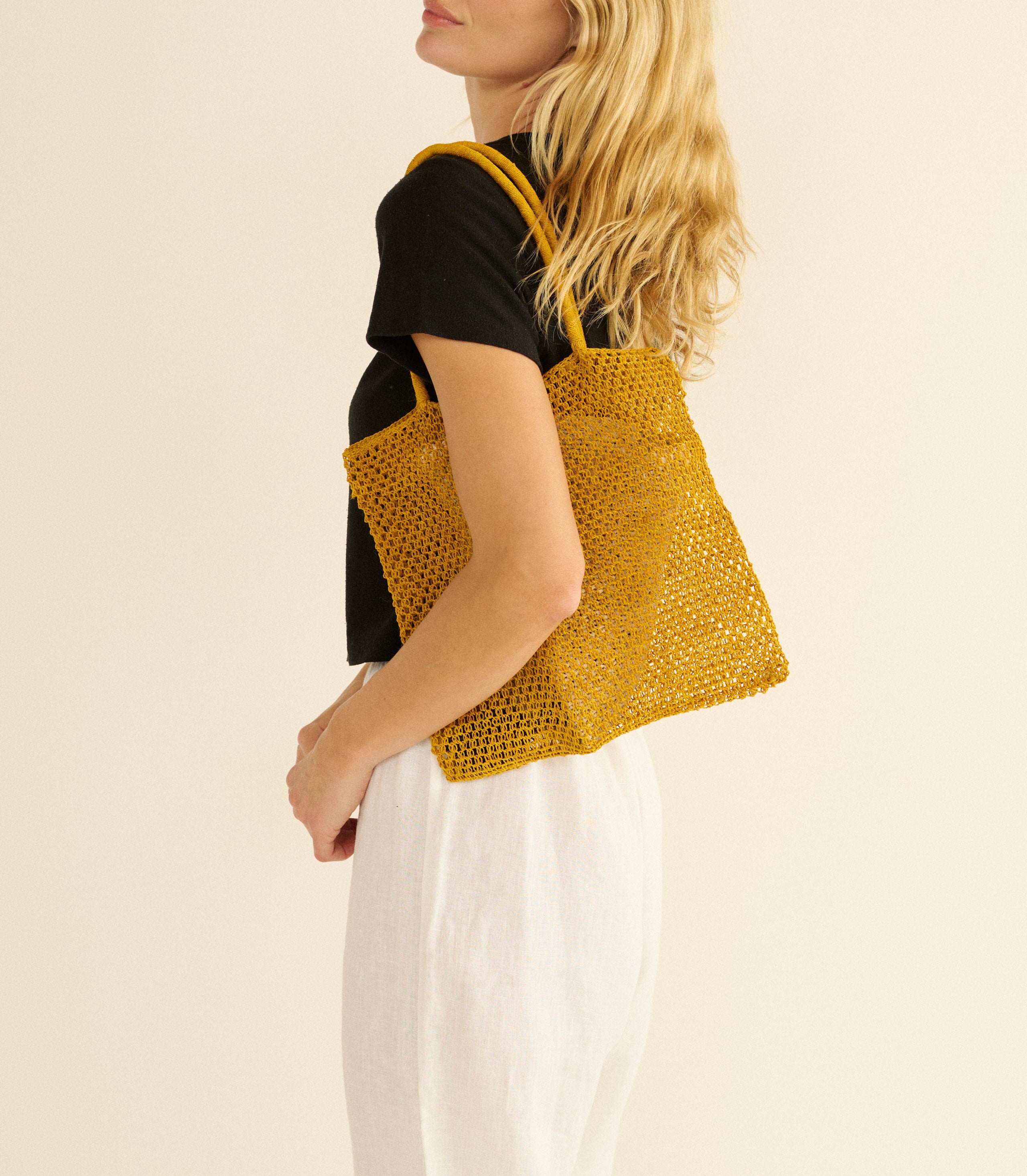 Woman holding a yellow knitted tote bag against a beige background