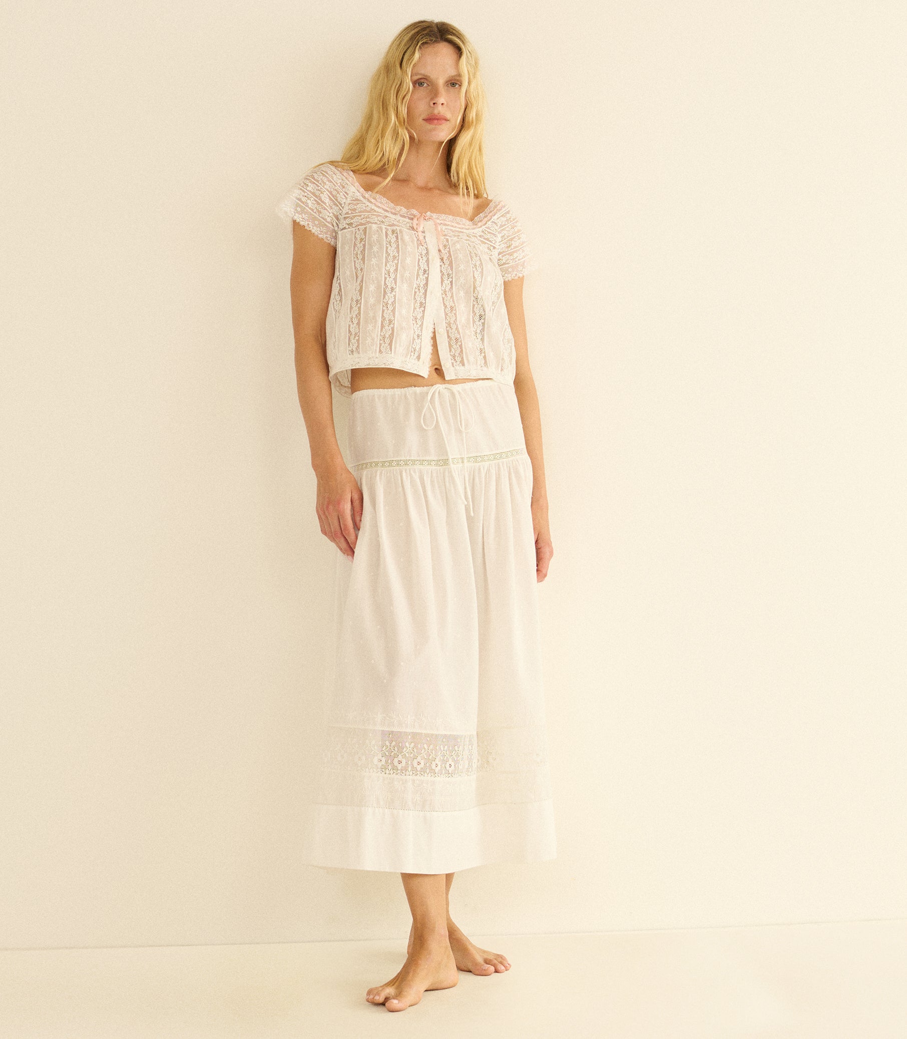 Woman wearing a white lace top and skirt set on a beige background