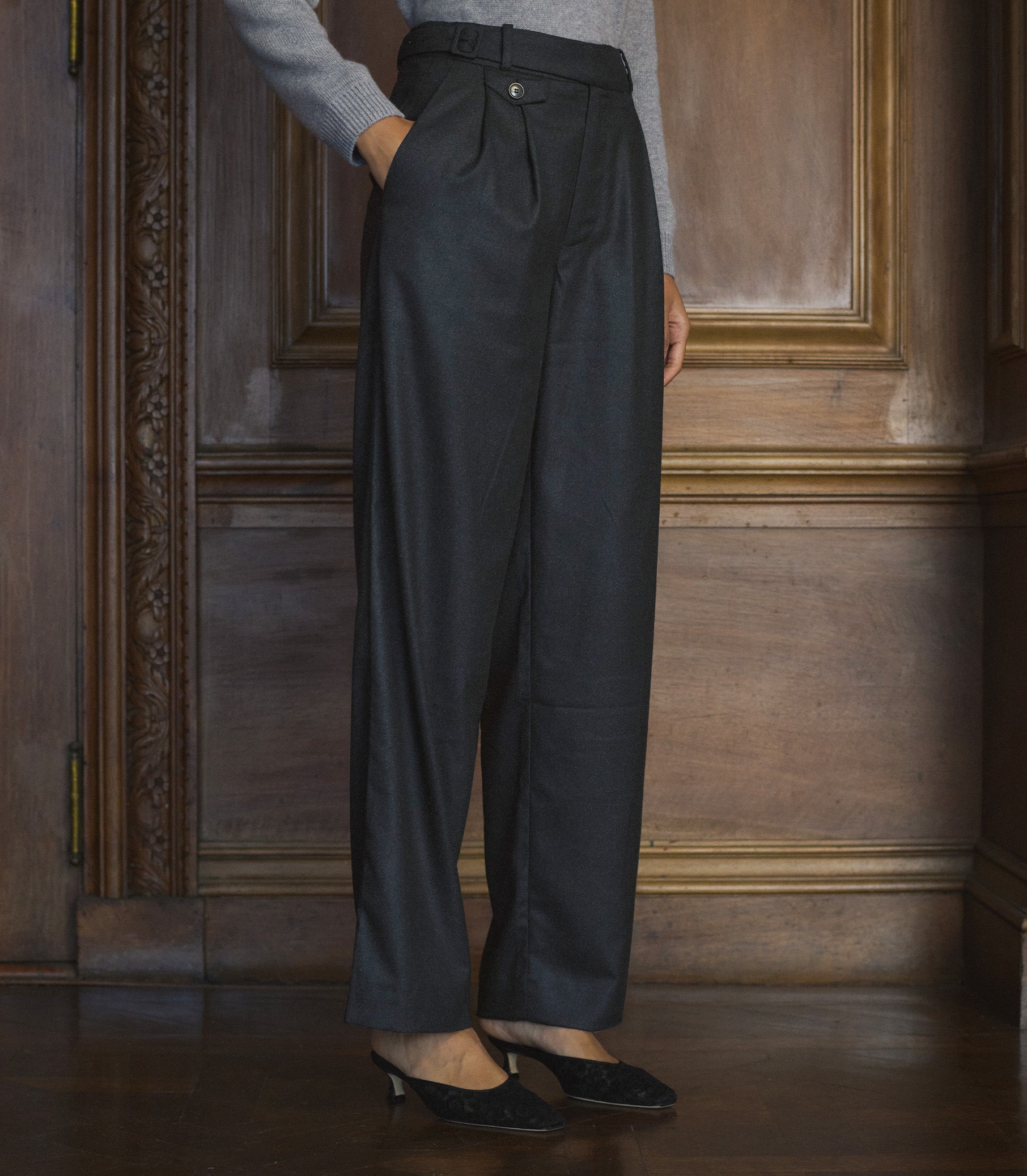 Person wearing dark gray wide-leg pants in a room with wooden paneling. 1