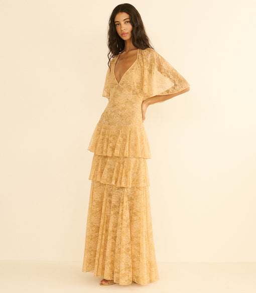 Woman wearing a gold tiered dress on a beige background