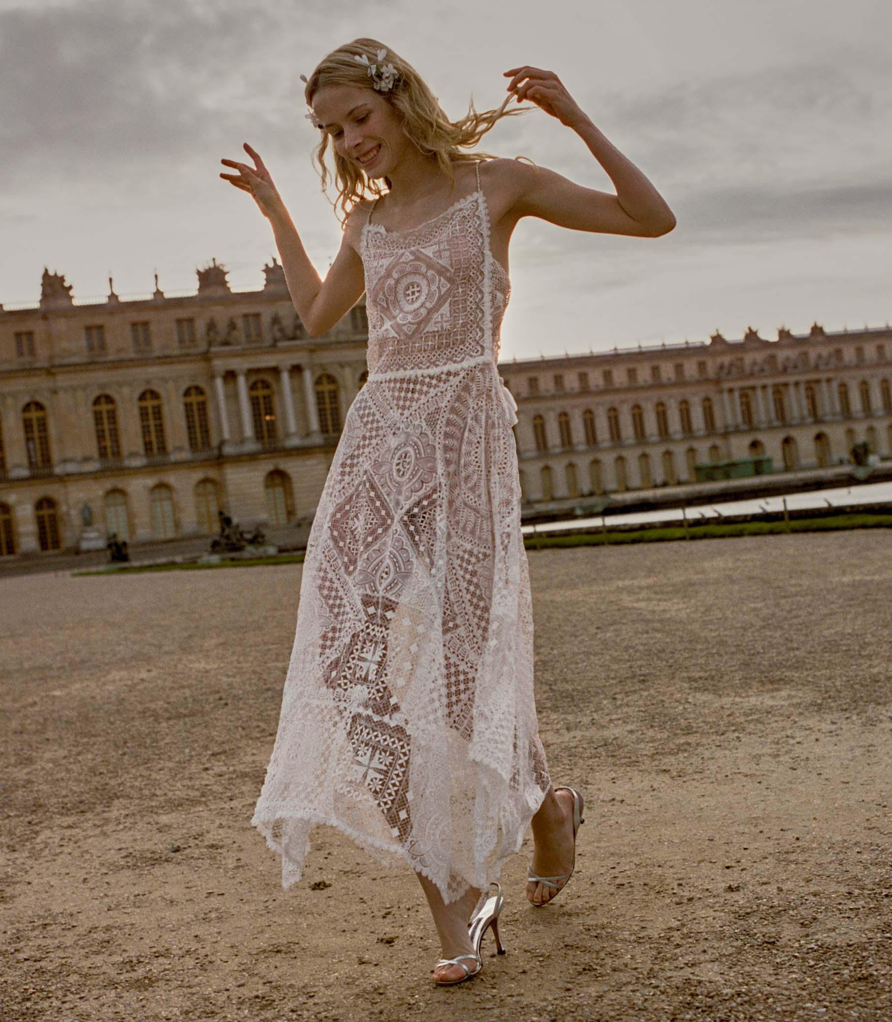 Woman wearing a white crochet dress standing in front of old buildings 1
