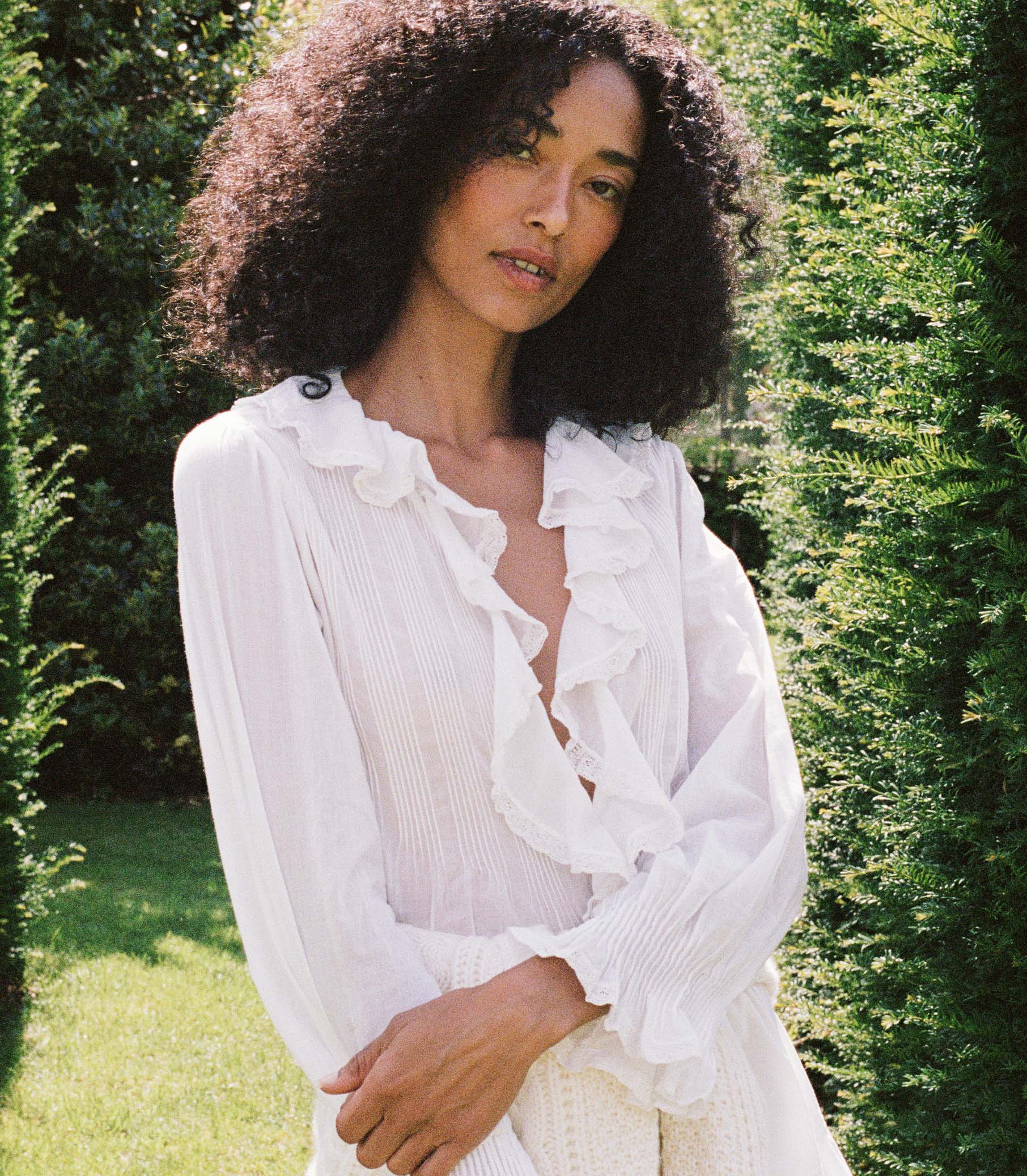 Woman wearing a white blouse and white skirt amongst greenery
