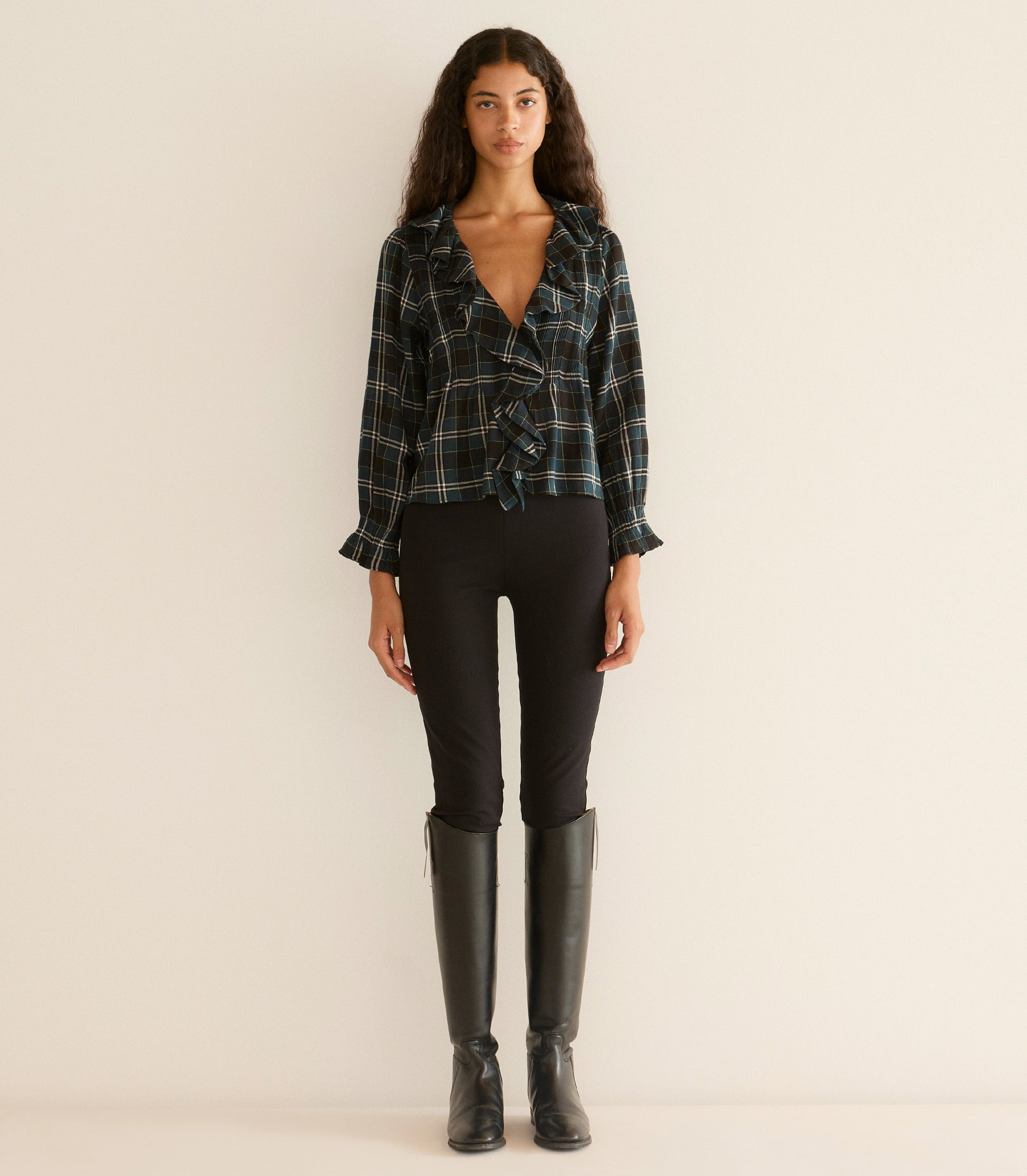 Woman wearing a plaid shirt, black leggings, and black knee-high boots on a beige background 5