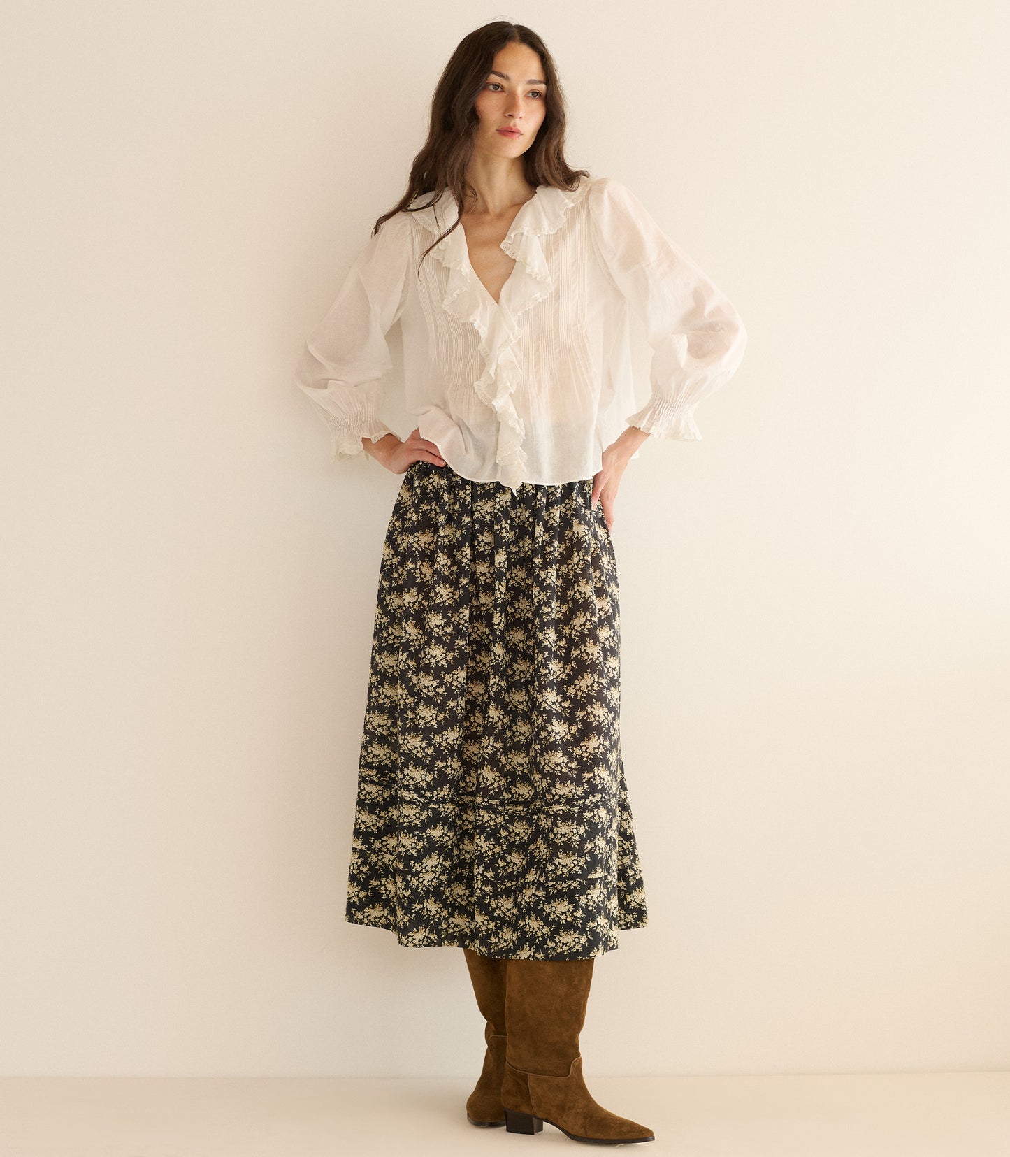 Woman wearing a white blouse and floral skirt against a plain background