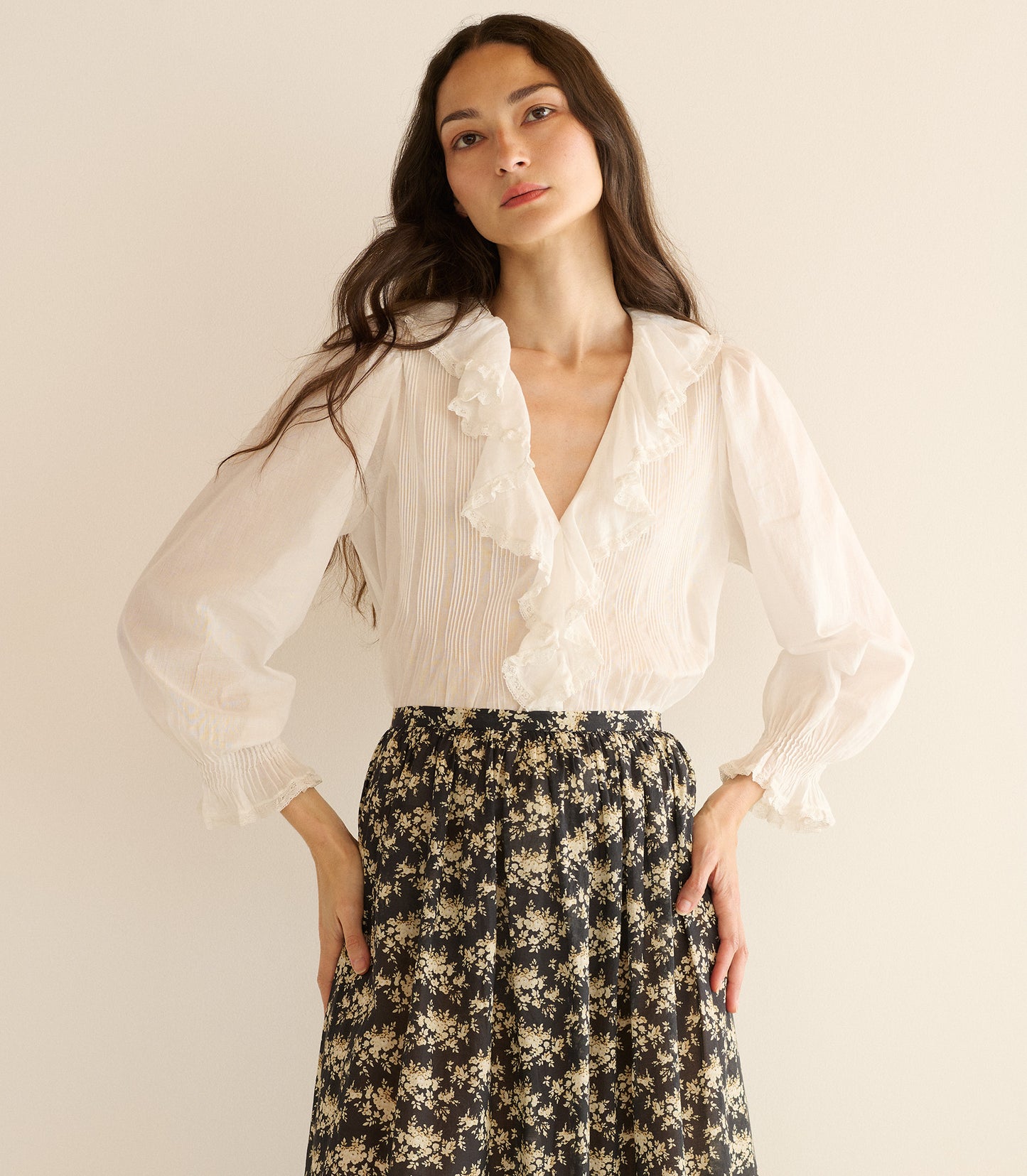 Woman wearing a white blouse and floral skirt against a plain background