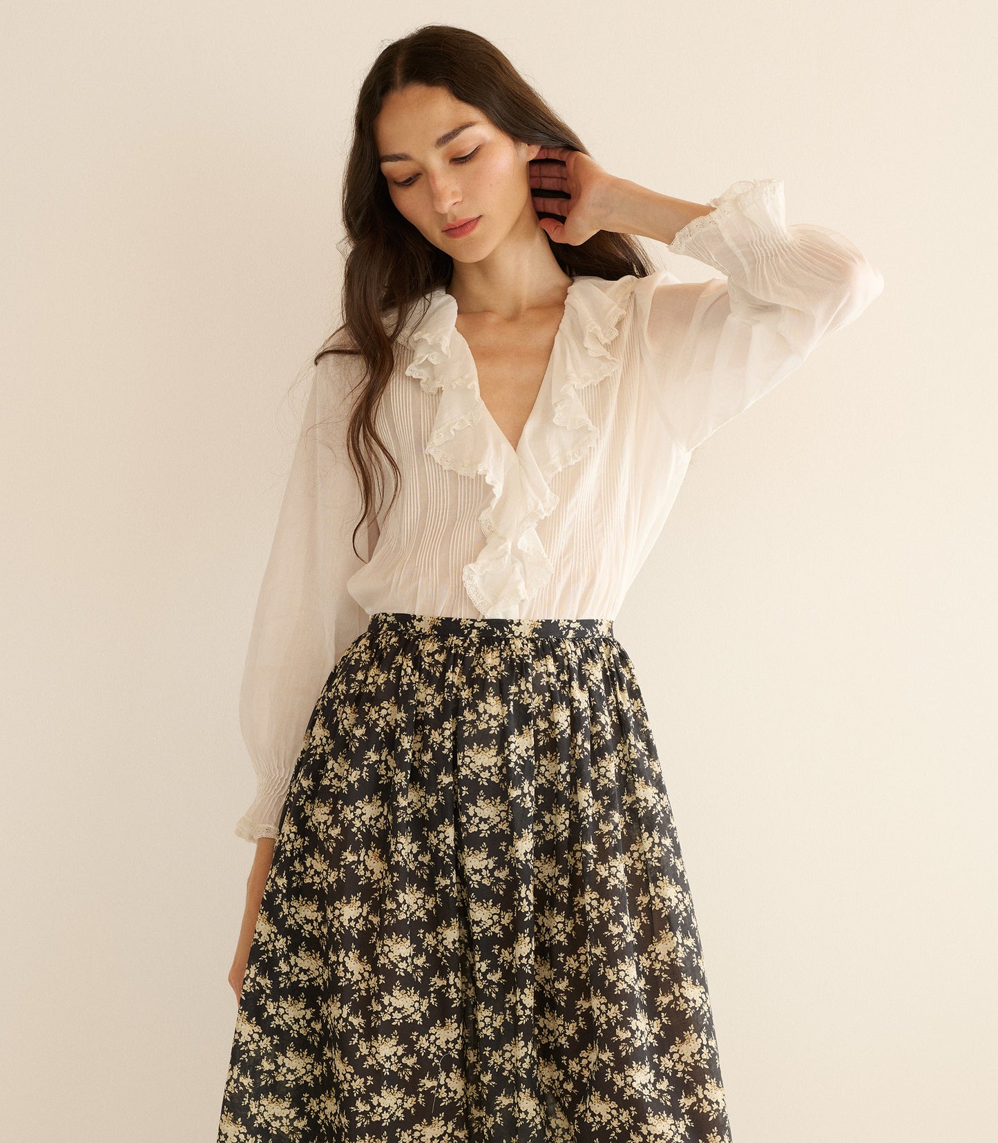 Woman wearing a white blouse and floral skirt against a plain background