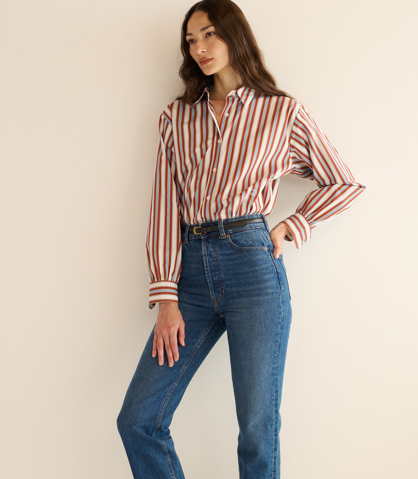 Woman wearing a striped shirt and blue jeans against a plain background
