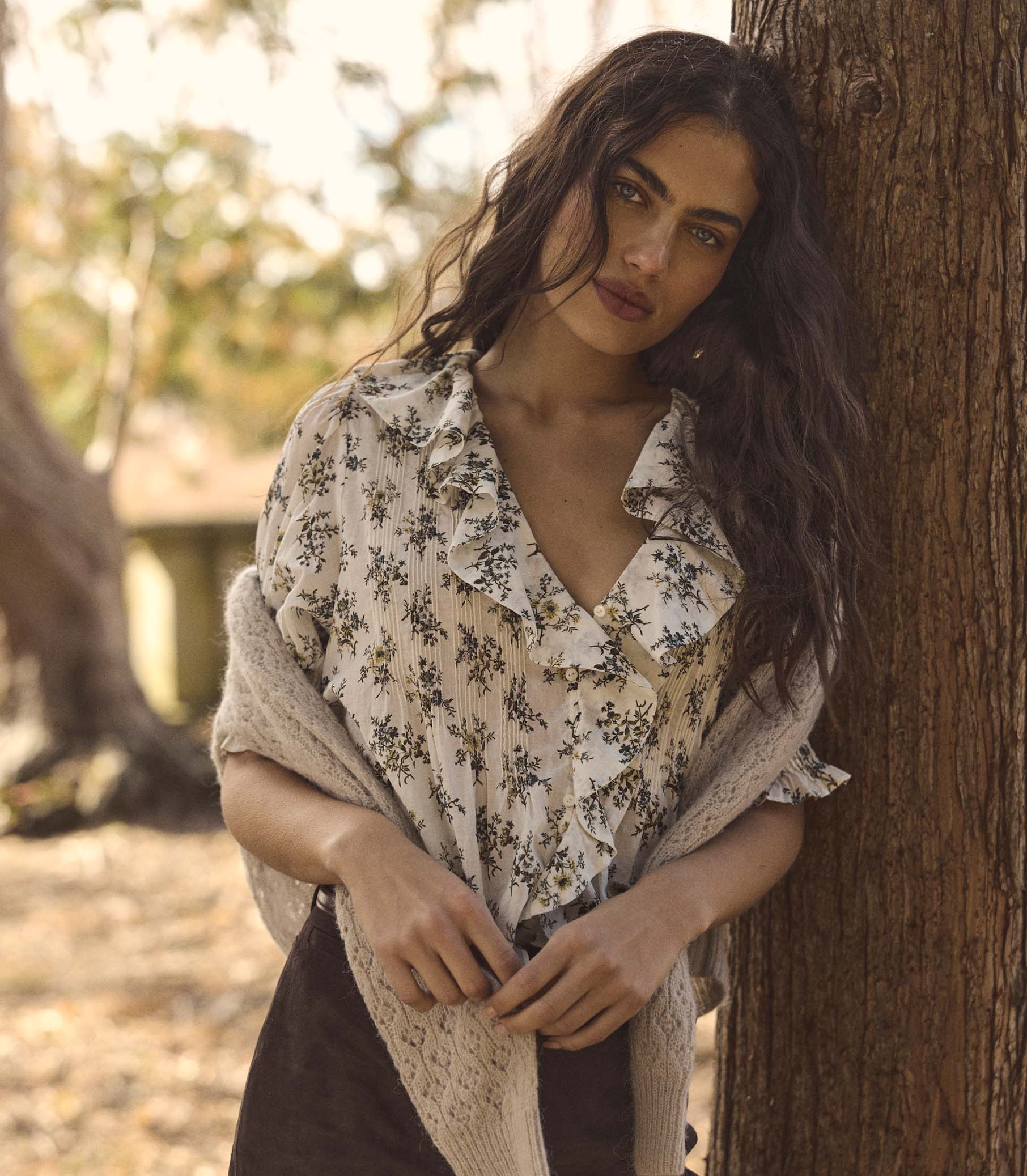 Woman in a floral blouse leaning against a tree in a natural setting 1