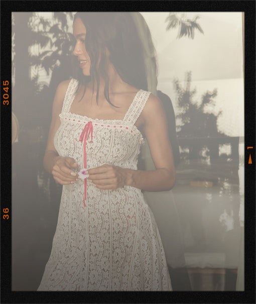 Woman in a white lace dress holding a small object outdoors with a blurred background