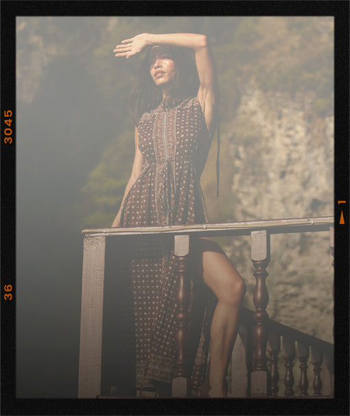 Woman in a patterned dress standing on a wooden bench with a blurred natural background