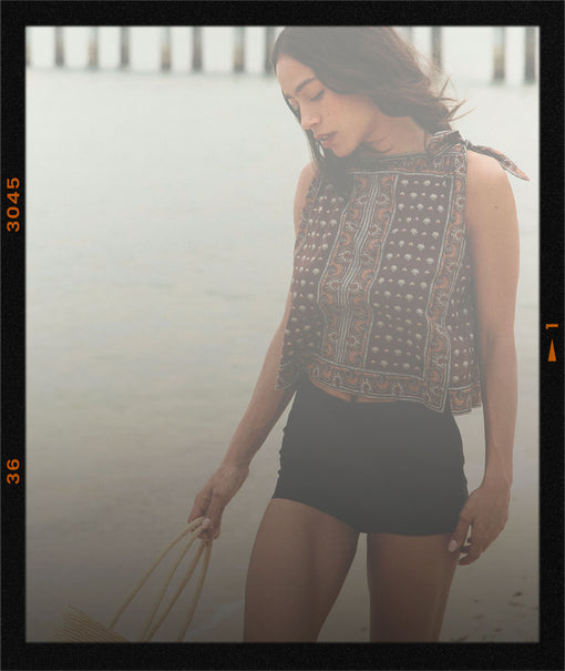 Woman wearing a brown paisley top with black shorts walking on the beach.