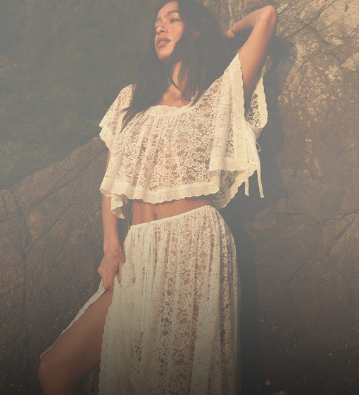 Woman in a white lace outfit standing against a textured wall.