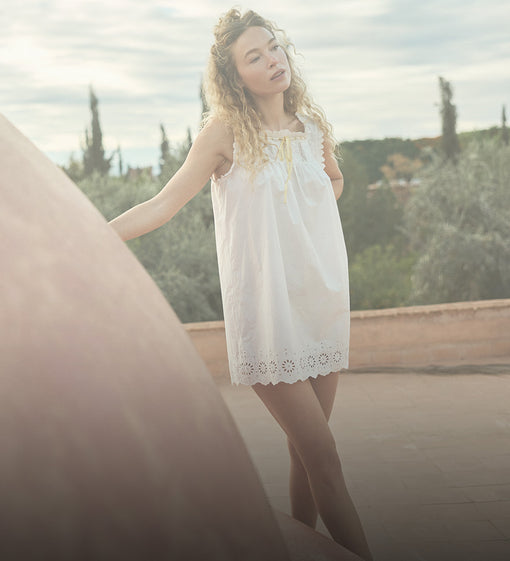 Woman in a white dress standing outdoors with greenery in the background