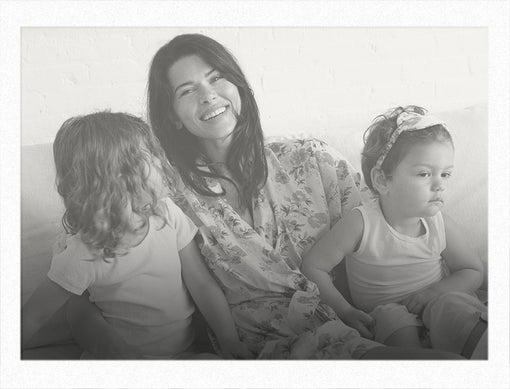 Woman sitting with two children on a couch, all smiling.