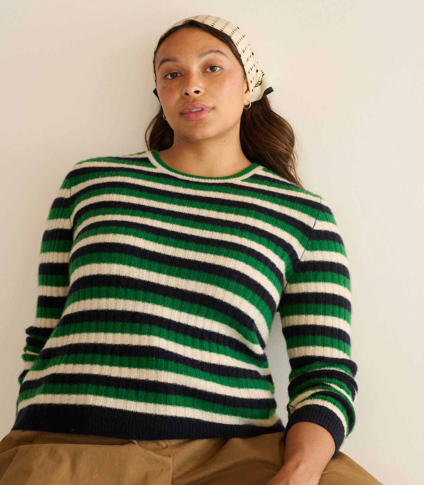 Person wearing a green and black striped sweater on a plain background