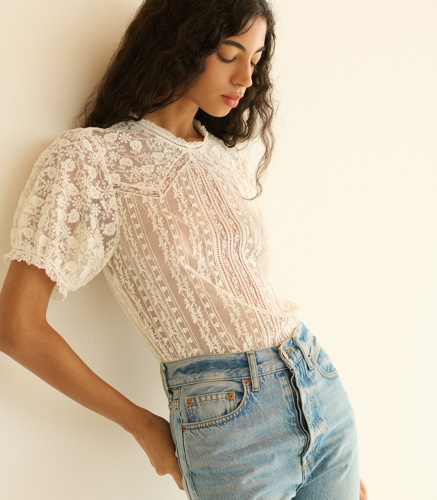 Woman wearing a lace top and jeans against a plain background