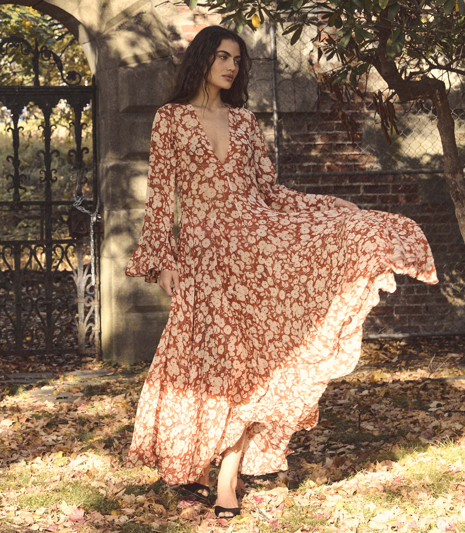 Woman in a red floral dress standing outdoors with trees and a gate in the background