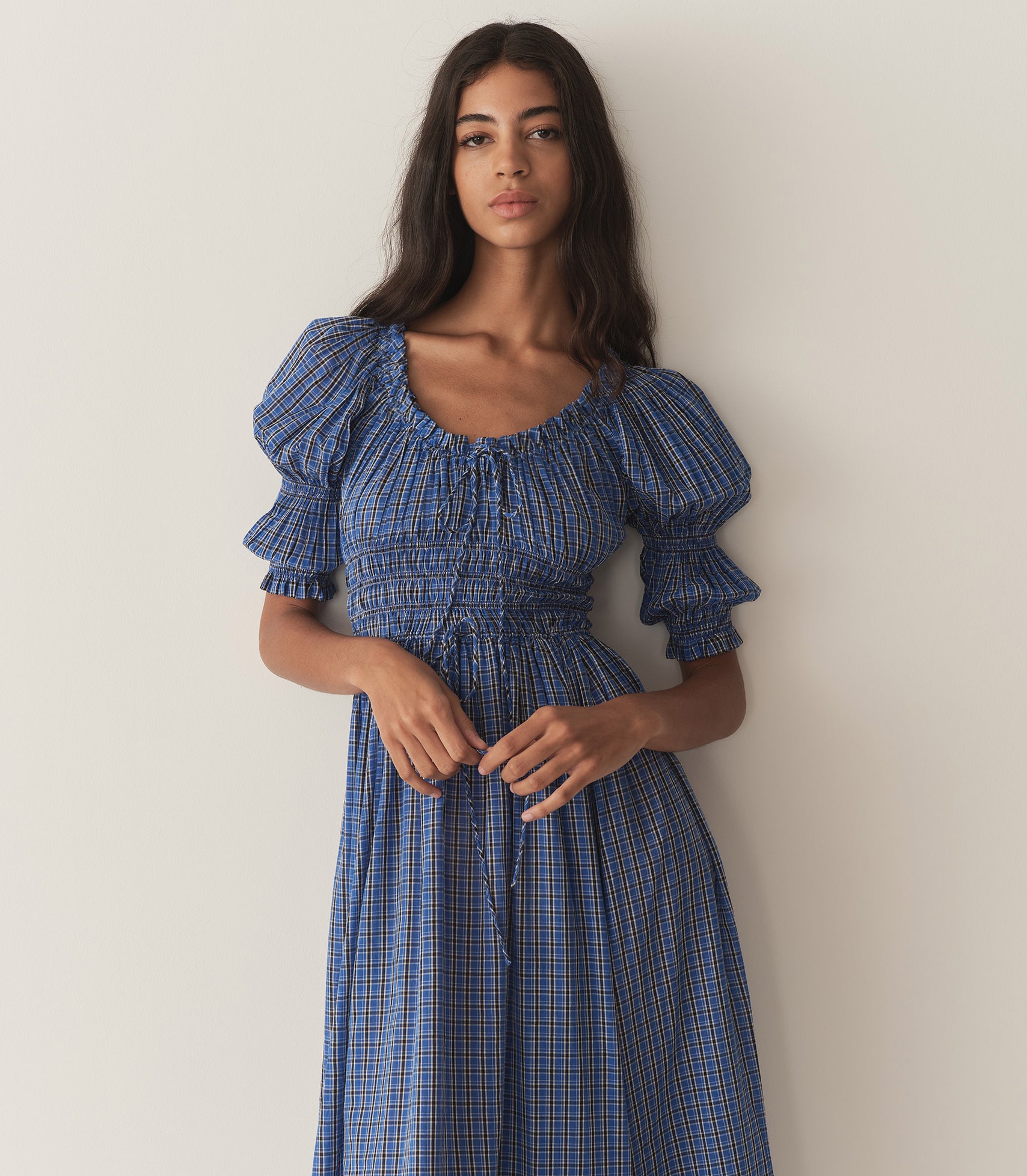 Rocio is wearing a long blue check dress with half puff sleeves and black flats.