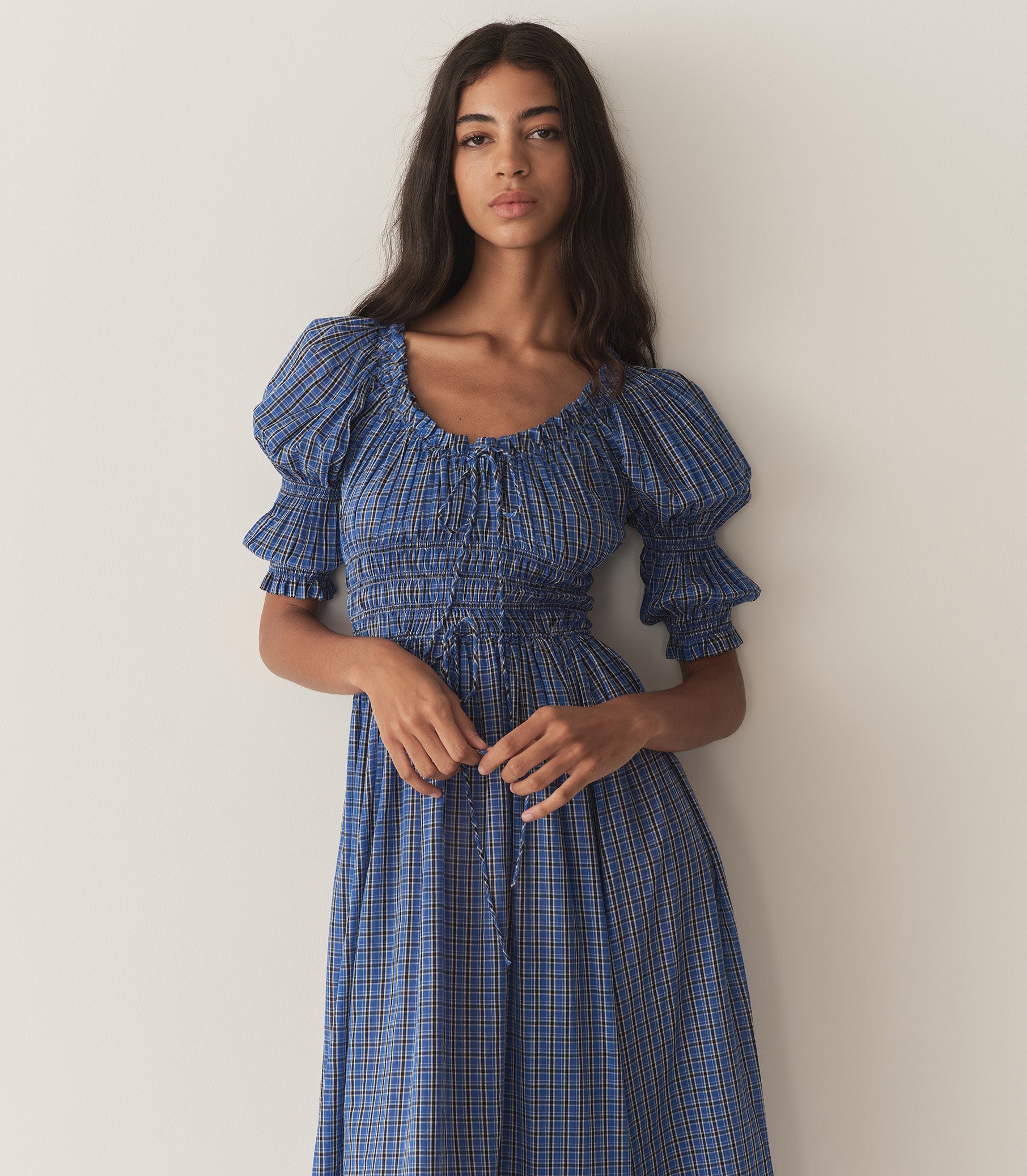 Rocio is wearing a long blue check dress with half puff sleeves and black flats.