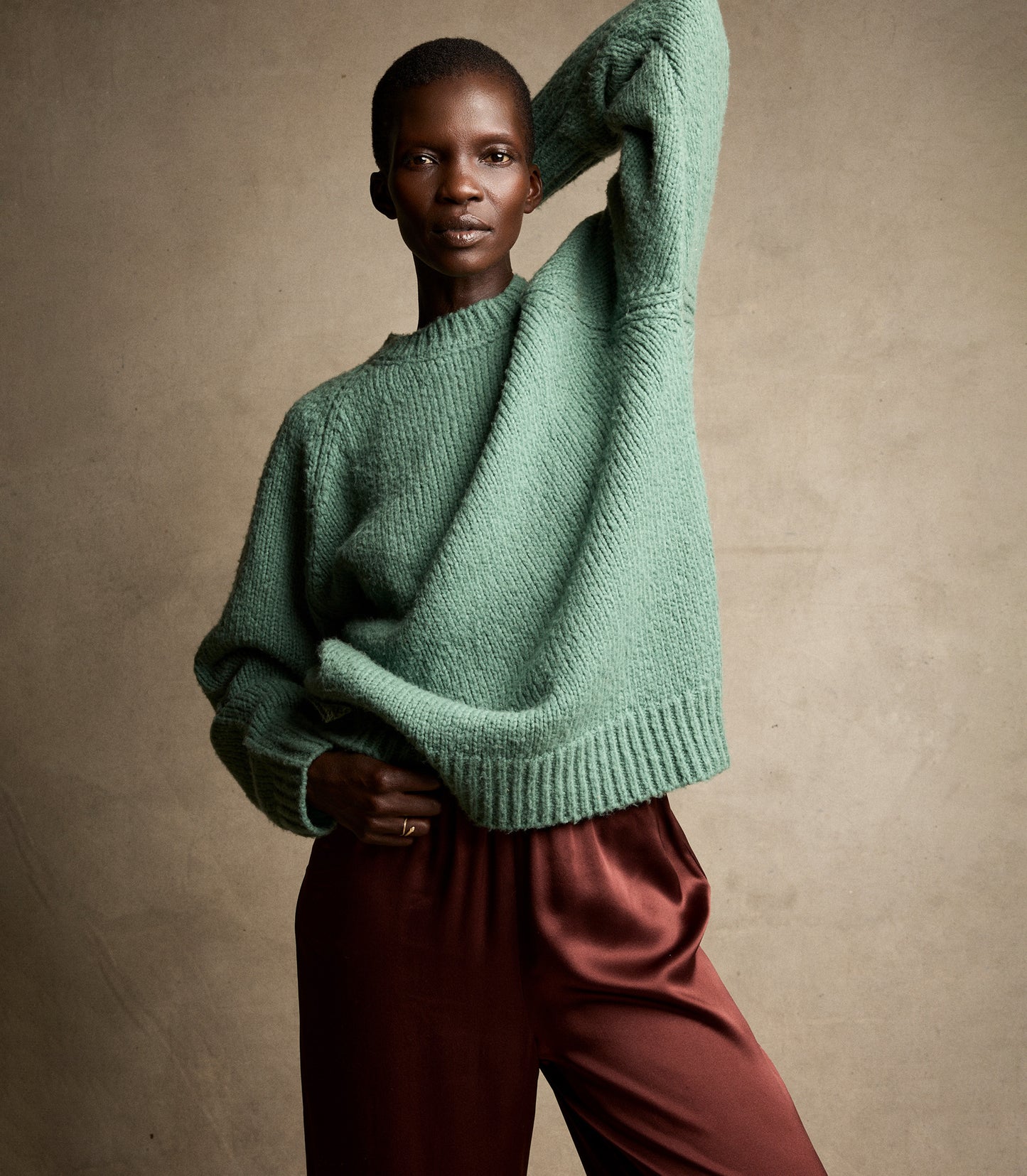 Person wearing a green sweater and maroon pants against a beige background