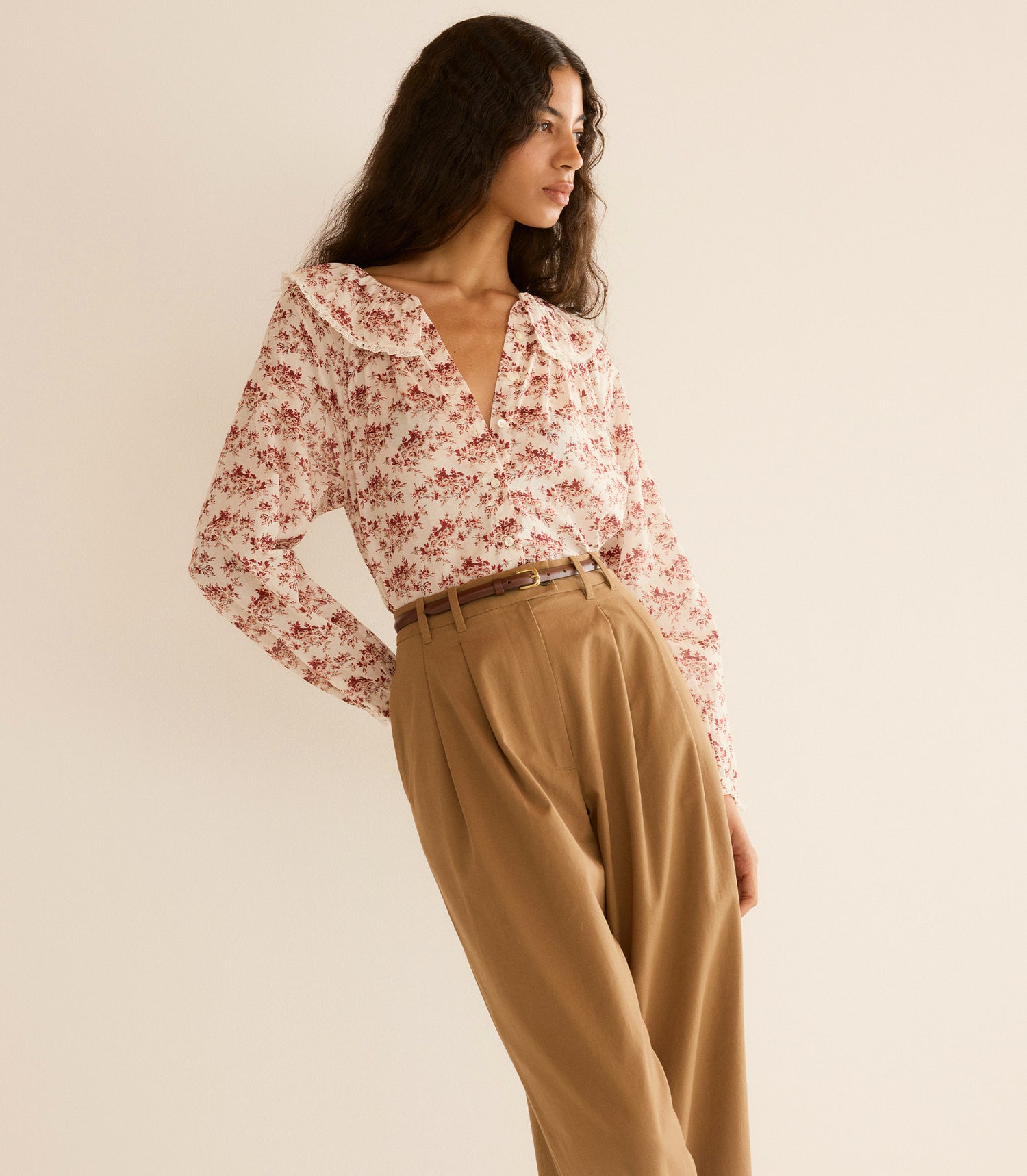 Woman wearing a floral blouse and beige pants against a beige background