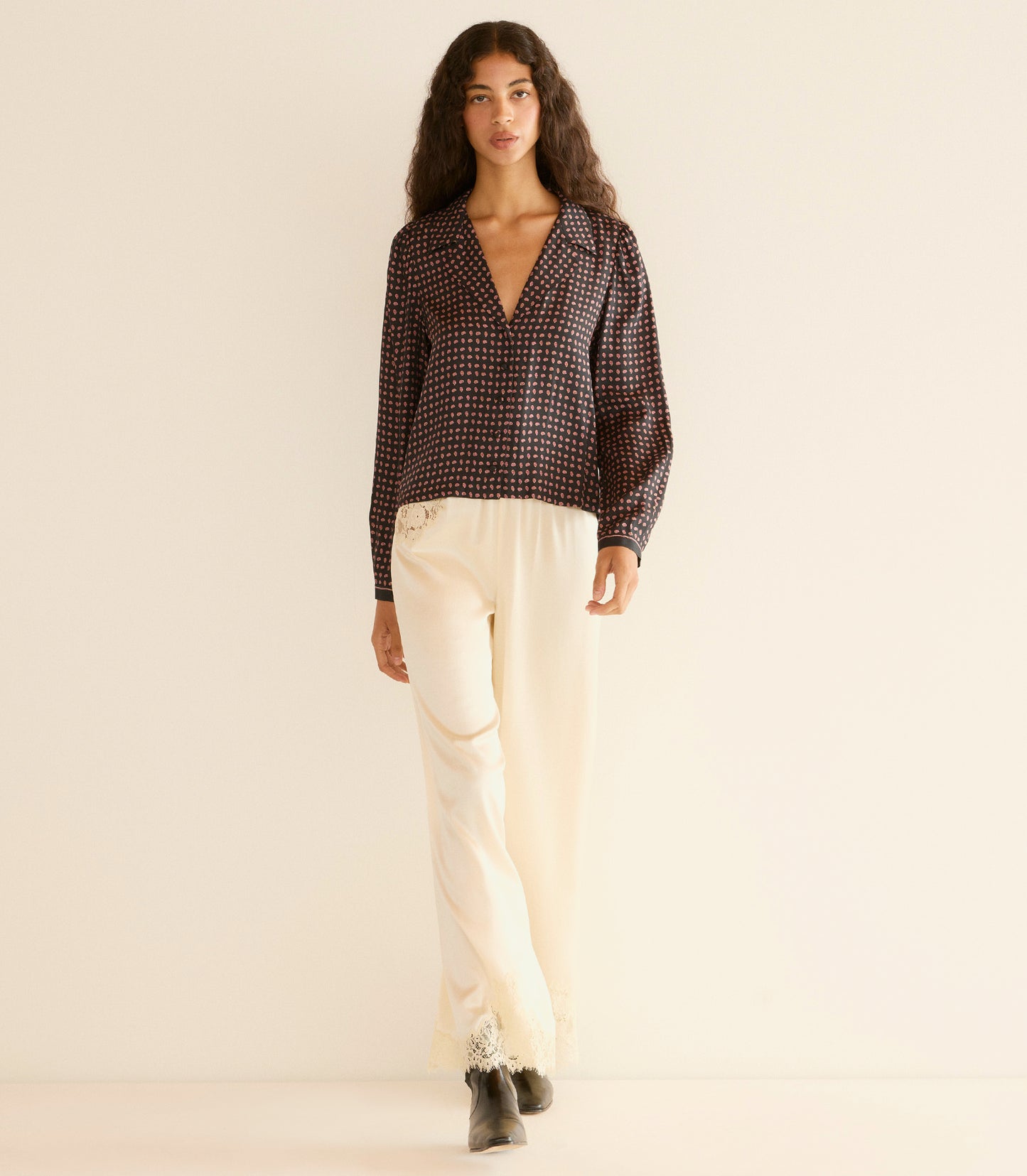 Woman wearing a black patterned blouse and beige pants on a beige background